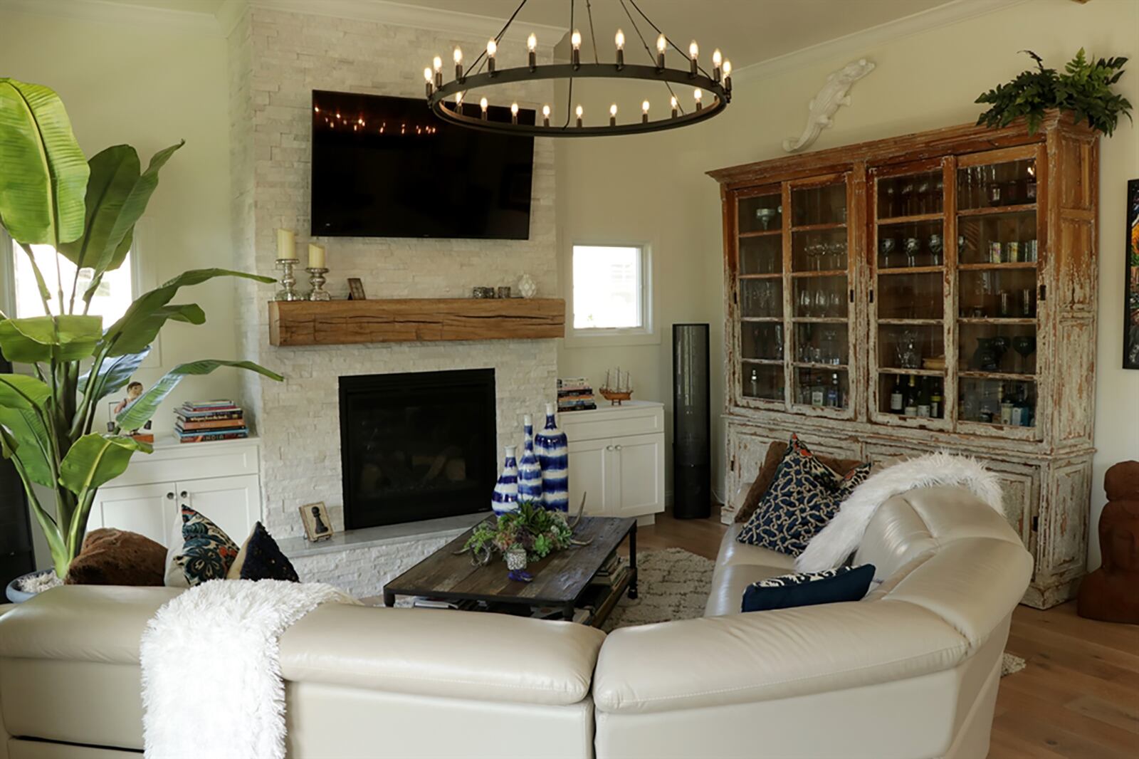 Lighting creates the social space designs of the living room, dining room and kitchen. To the left is the living room with a white stone gas fireplace as the centerpiece. The fireplace has a reclaimed wood mantel and a marble capped raised hearth. Built-in white cabinets flank the fireplace and have square windows above. CONTRIBUTED PHOTO BY KATHY TYLER