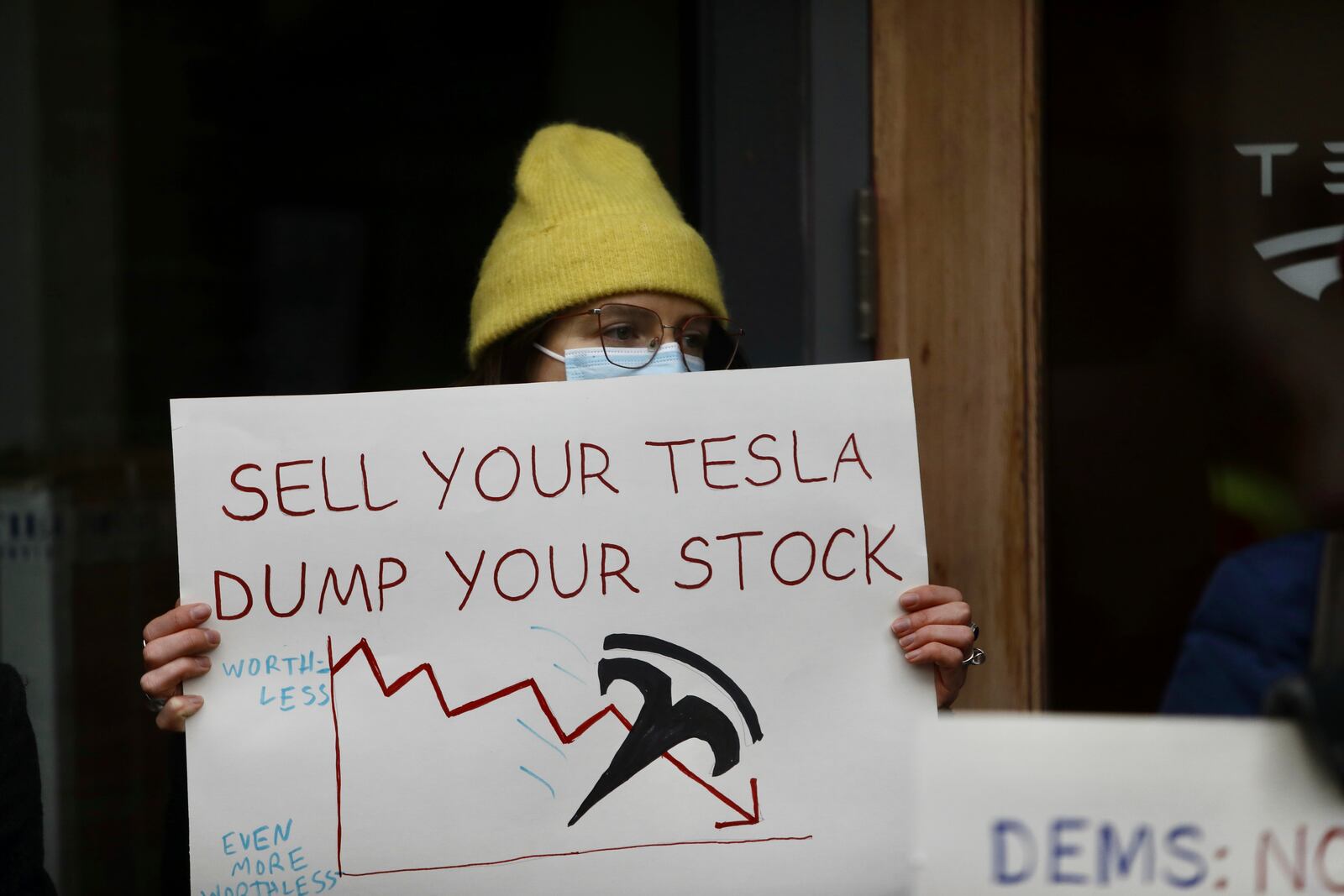 FILE - A person protesting Elon Musk's actions in the Trump administration holds a sign outside a Tesla showroom in Seattle, Thursday, Feb. 13, 2025. (AP Photo/Manuel Valdes, File)