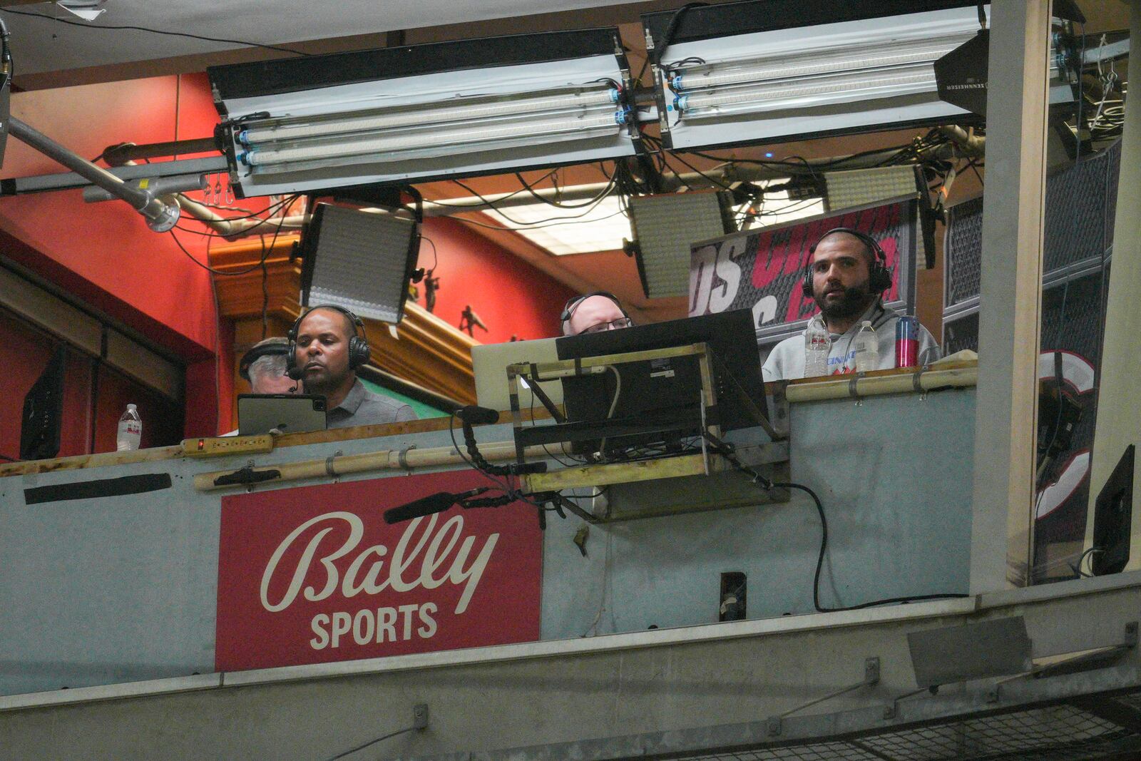 FILE - Cincinnati Reds' Joey Votto, right, sits in the broadcast booth with John Sadak, center right, and Barry Larkin, center left, during a baseball game against the St. Louis Cardinals Wednesday, Aug. 31, 2022, in Cincinnati. Amazon will partner with the Diamond Sports as part of a restructuring agreement as the largest owner of regional sports networks looks to emerge from bankruptcy. Diamond owns 18 networks under the Bally Sports banner. Those networks have the rights to 37 professional teams — 11 baseball, 15 NBA and 11 NHL.(AP Photo/Jeff Dean, File)