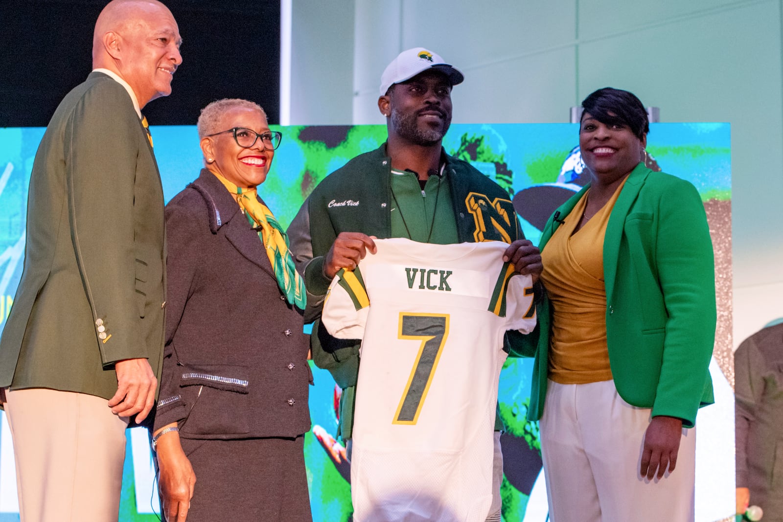 Michael Vick holds up a number seven Norfolk State jersey with his name on it after he is introduced as the head coach by Norfolk State President Javaune Adams-Gaston, second from left, Bishop Kim Brownand, left, and Director of Athletics Dr. Melody Webb, right, during a press conference on Monday, Dec. 23, 2024 in Norfolk, Va. (AP Photo/Mike Caudill)