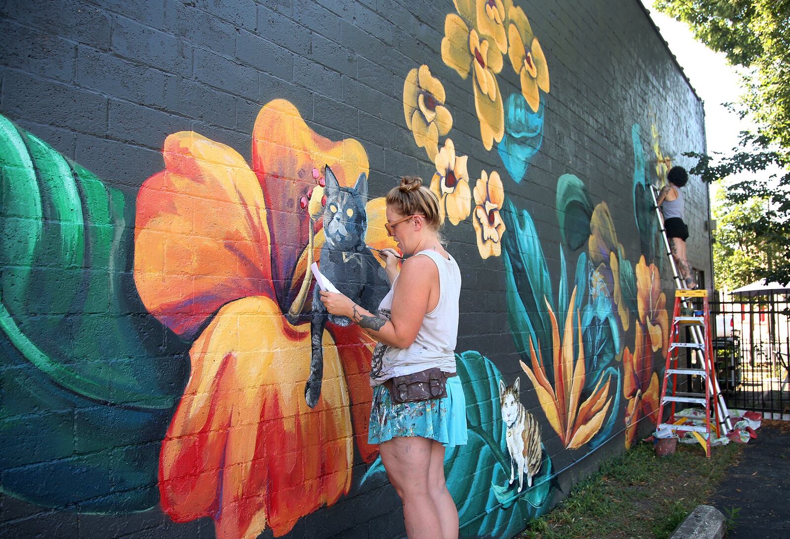 Tiffany Clark (left) and Leslea Hipp (right) of the Mural Machine is creating a mural of cats on the side of Lily’s Bistro in Dayton’s Oregon District. People who pay a fee will be able to submit pictures of their cats for realistic paintings on the west side of the restaurant. The project is a fundraiser for local groups dedicated to animal welfare. So far, 40 cats are committed to the project. There is room for 85 feline portraits. LISA POWELL / STAFF