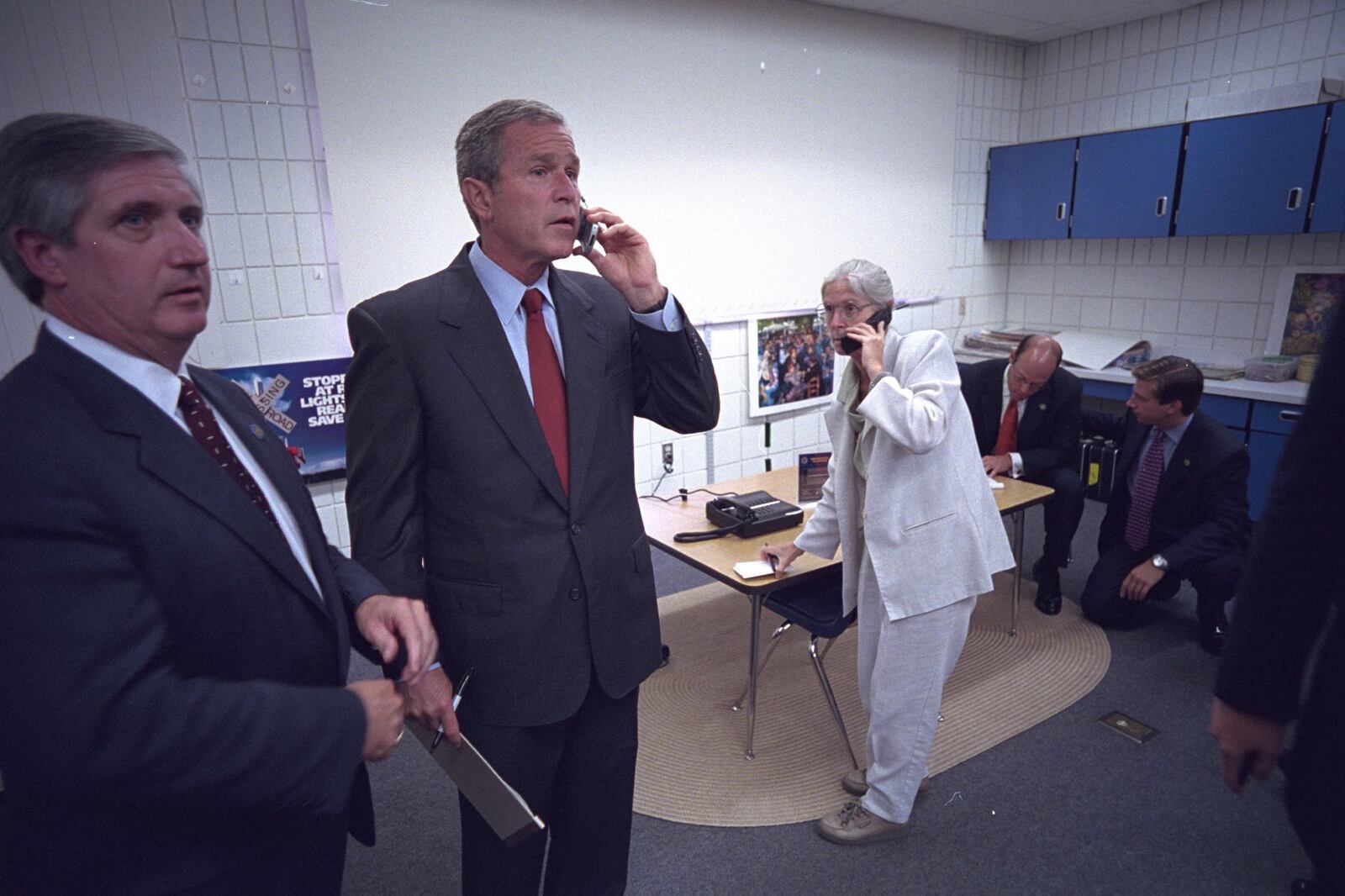 President George W. Bush talks on the phone wtih Vice President Dick Cheney, New York Gov. George Pataki and FBI Director Robert Mueller, from Emma E. Holder Elementary School on Sept. 11, 2001. At left is Andrew Card, White House chief of staff, and in the background is Deborah Loewer, then director of the White House Situation Room. White House photo by Eric Draper