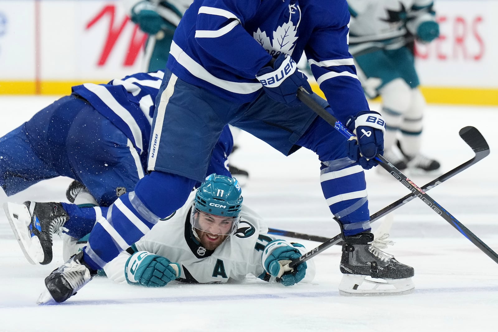 San Jose Sharks forward Luke Kunin (11) is taken down by Toronto Maple Leafs defenseman Conor Timmins, left, during third-period NHL hockey game action in Toronto, Monday, March 3, 2025. (Nathan Denette/The Canadian Press via AP