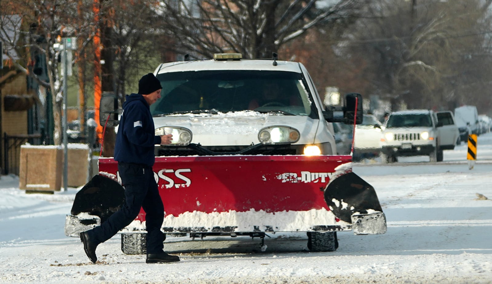 A pedestrian crosses as a pickup truck equipped with a snow plow waits at the traffic signal after a winter storm plunged daytime high temperatures into the single digits and left up to six inches of snow in its wake Monday, Jan. 20, 2025, in Denver. (AP Photo/David Zalubowski)