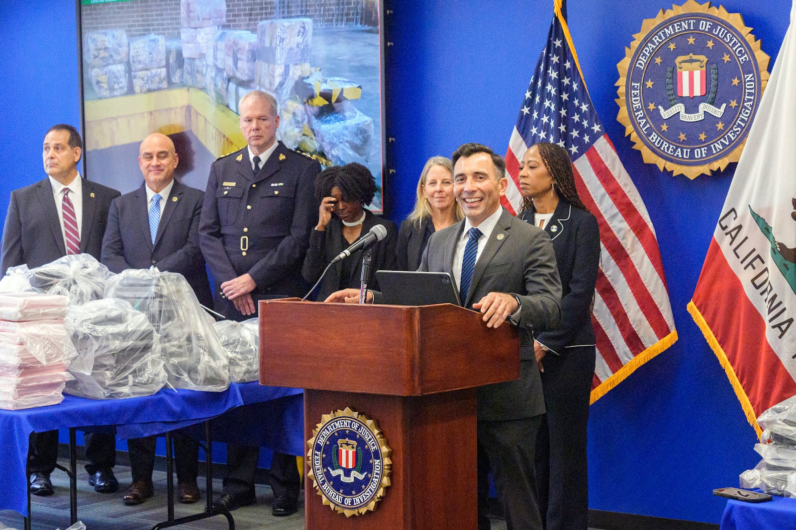 United States Attorney Martin Estrada, at podium, smiles as he's joined by federal, local, and international officials, to announce federal charges and arrests of alleged members of a transnational drug trafficking operation that routinely shipped hundreds of kilograms of cocaine from Colombia, through Mexico and Southern California, to Canada and other locations in the United States, during a news conference at the FBI offices in Los Angeles, Thursday, Oct. 17, 2024. (AP Photo/Damian Dovarganes)