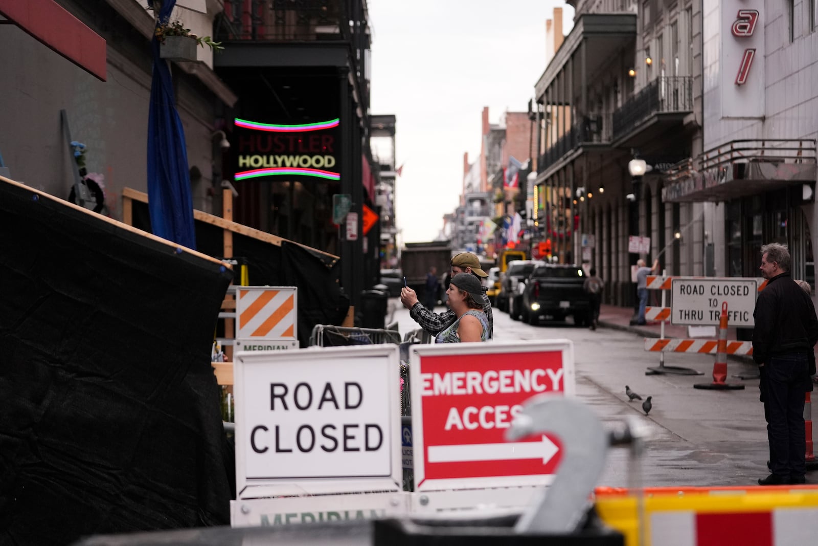 People visit a memorial for victims of the Jan. 1 car attack next to newly installed security barriers on Bourbon Street ahead of the Super Bowl in New Orleans, Friday, Jan. 31, 2025. (AP Photo/Gerald Herbert)