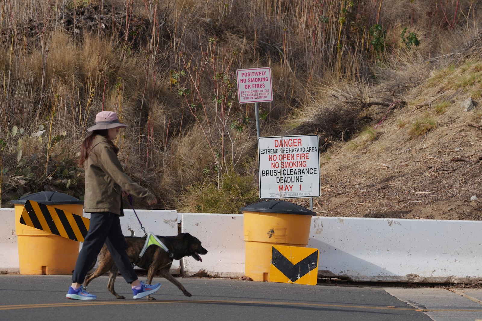 A Duarte resident walks her dog past a sign of an extreme fire hazard area Friday, Jan. 31, 2025, in Duarte, Calif. (AP Photo/Damian Dovarganes)