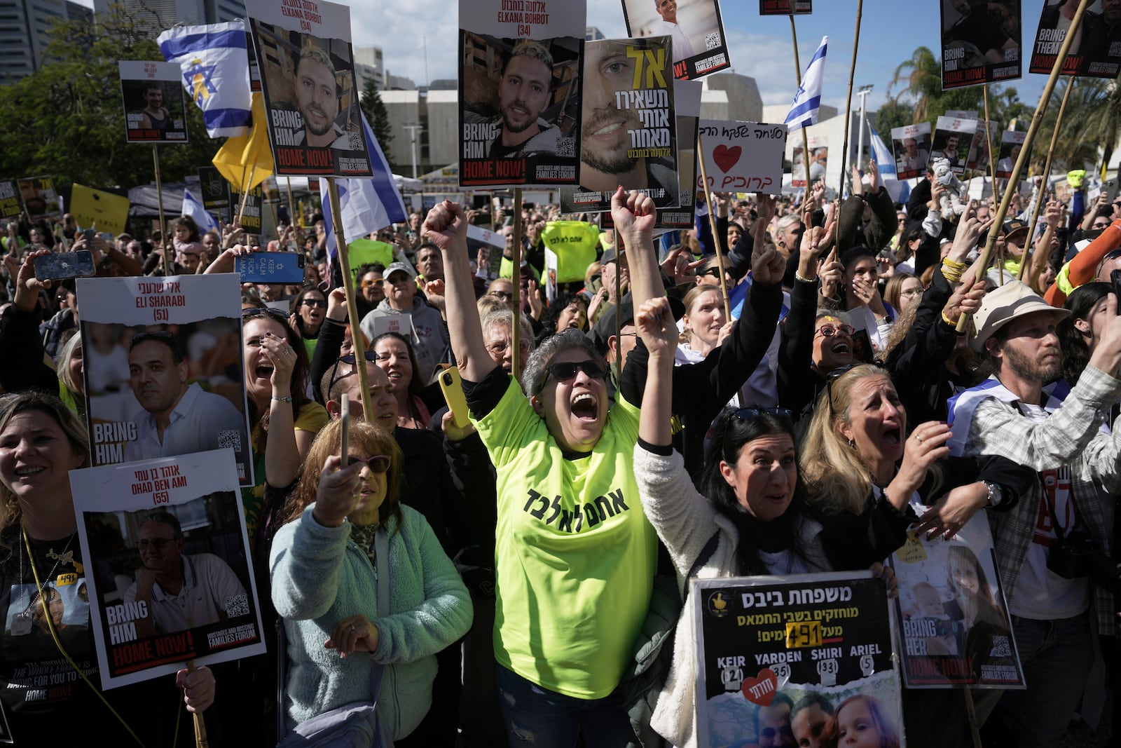 People holding posters with photos of Israelis hostages Eli Sharabi, Or Levy and Ohad Ben Ami, react at the so-called "hostages square" as they watch their release live on a television screen in Tel Aviv, Israel on Saturday, Feb. 8, 2025. (AP Photo/Oded Balilty)