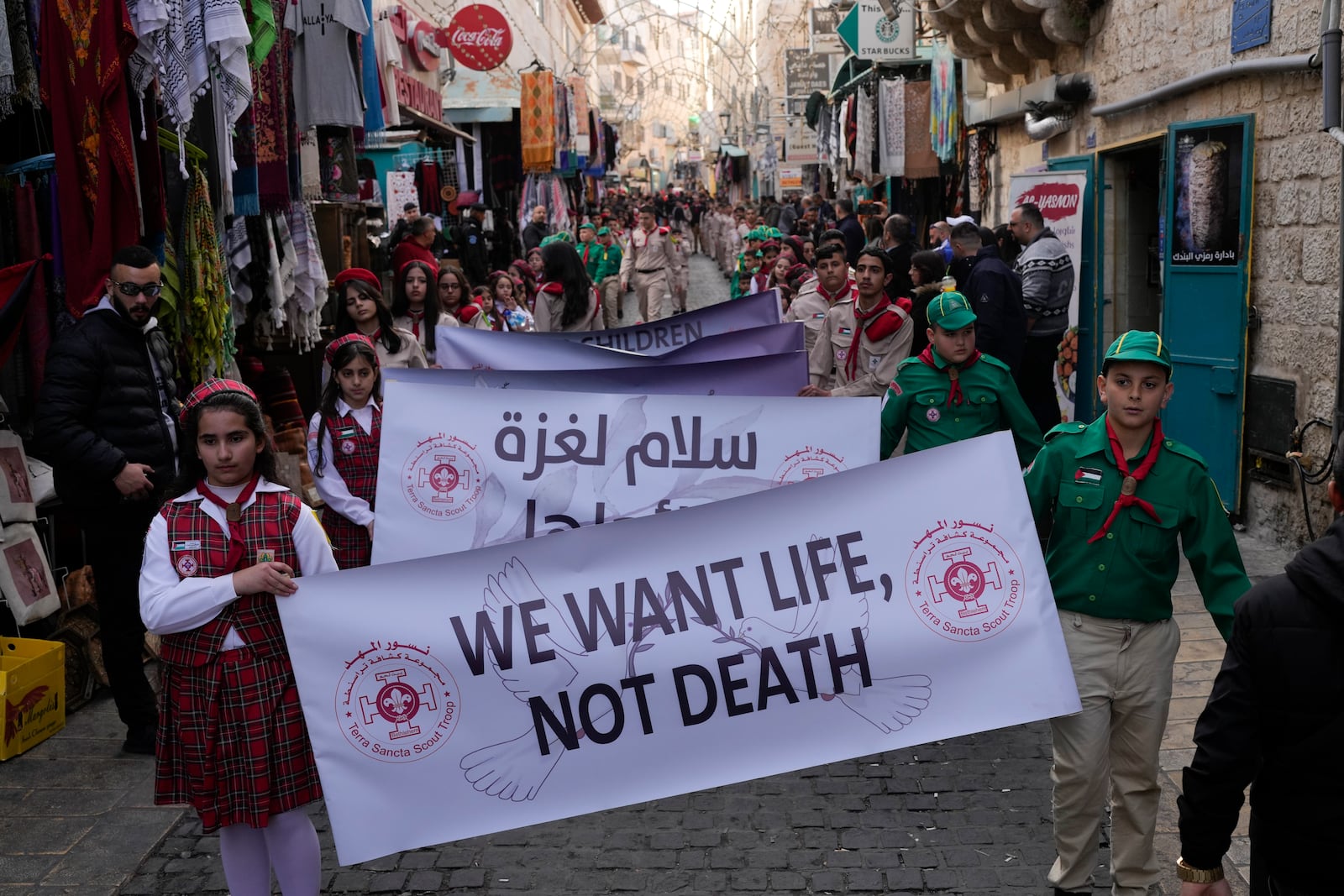 Scouts hold a sign that reads "We want life, not death" during the traditional Christian procession towards the Church of the Nativity, traditionally believed to be the birthplace of Jesus, on Christmas Eve, in the West Bank city of Bethlehem, Tuesday, Dec. 24, 2024. (AP Photo/Matias Delacroix)