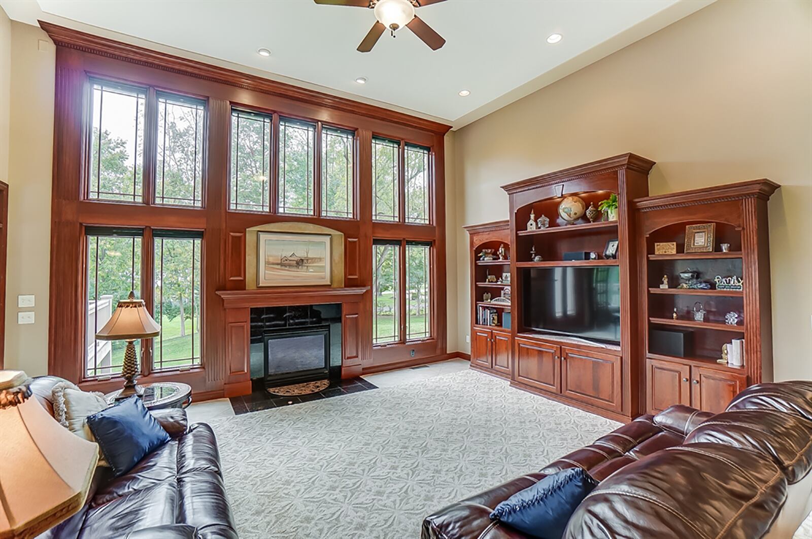 The great room has a wall of windows trimmed with fluted cherry woodwork that continues into a wall of built-in media cabinetry and display shelves. A granite, gas fireplace has an artwork nook above and a granite hearth. CONTRIBUTED PHOTO