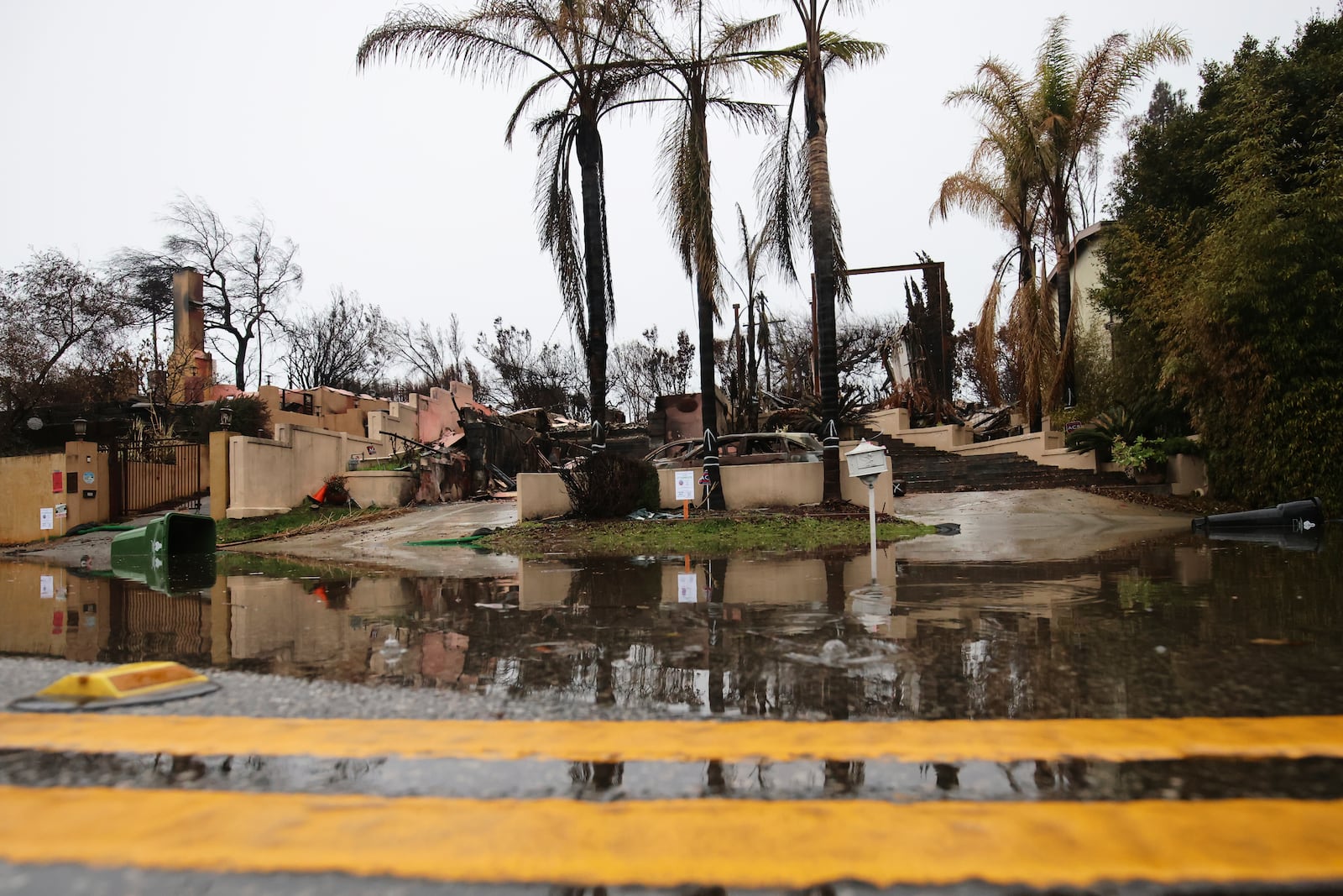 Water is reflected in front of a fire-ravaged property in the Palisades Fire zone during a storm Thursday, Feb. 13, 2025, in the Pacific Palisades neighborhood of Los Angeles. (AP Photo/Ethan Swope)