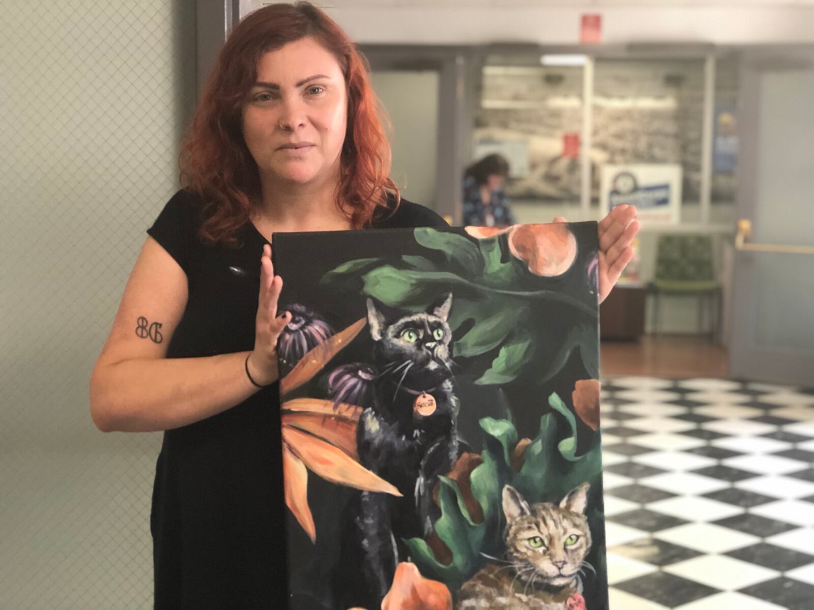 Emily Mendenhall, co-owner of Lily’s Bistro, holds up a painting of her late cat and another feline. Realistic cats will be painted on a mural on Lily’s west-facing wall. People can get portraits of their cats for a fee, a portion of which will go to animal welfare groups. CORNELIUS FROLIK / STAFF