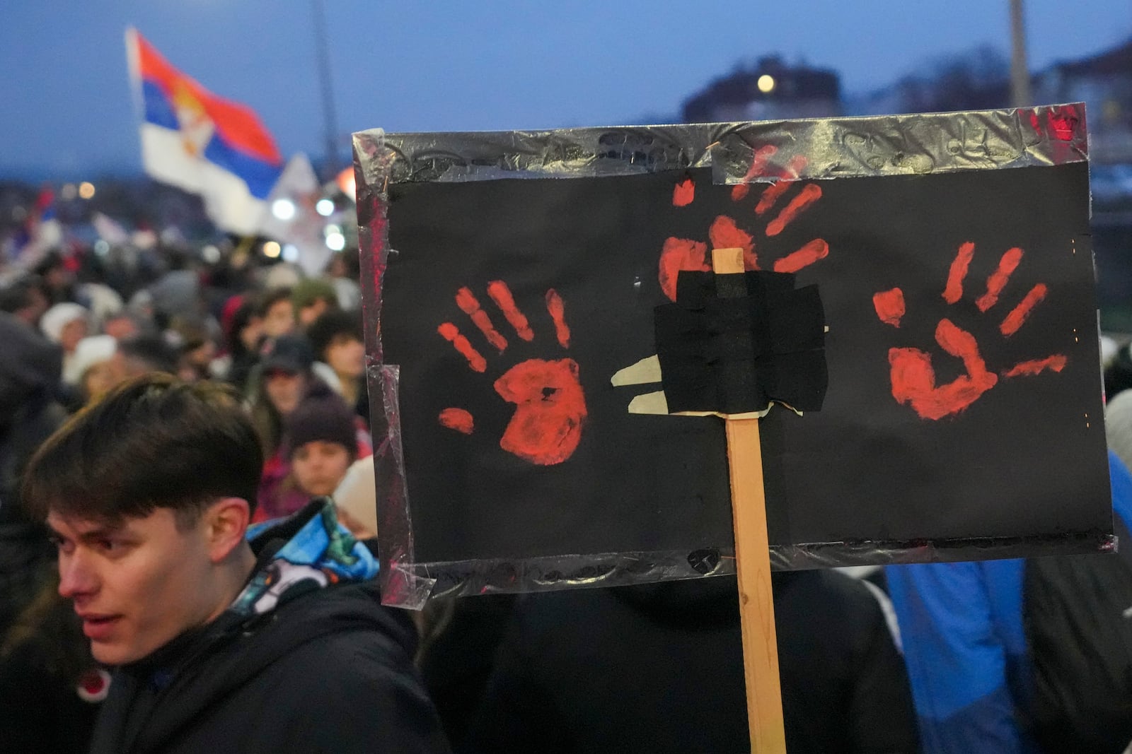 A man holds a banner with red hands symbolizing blood during a student-led large protest and a 15-hour blockade of the streets in Serbian industrial town of Kragujevac, to protest the deaths of 15 people killed in the November collapse of a train station canopy, Saturday, Feb. 15, 2025. (AP Photo/Darko Vojinovic)