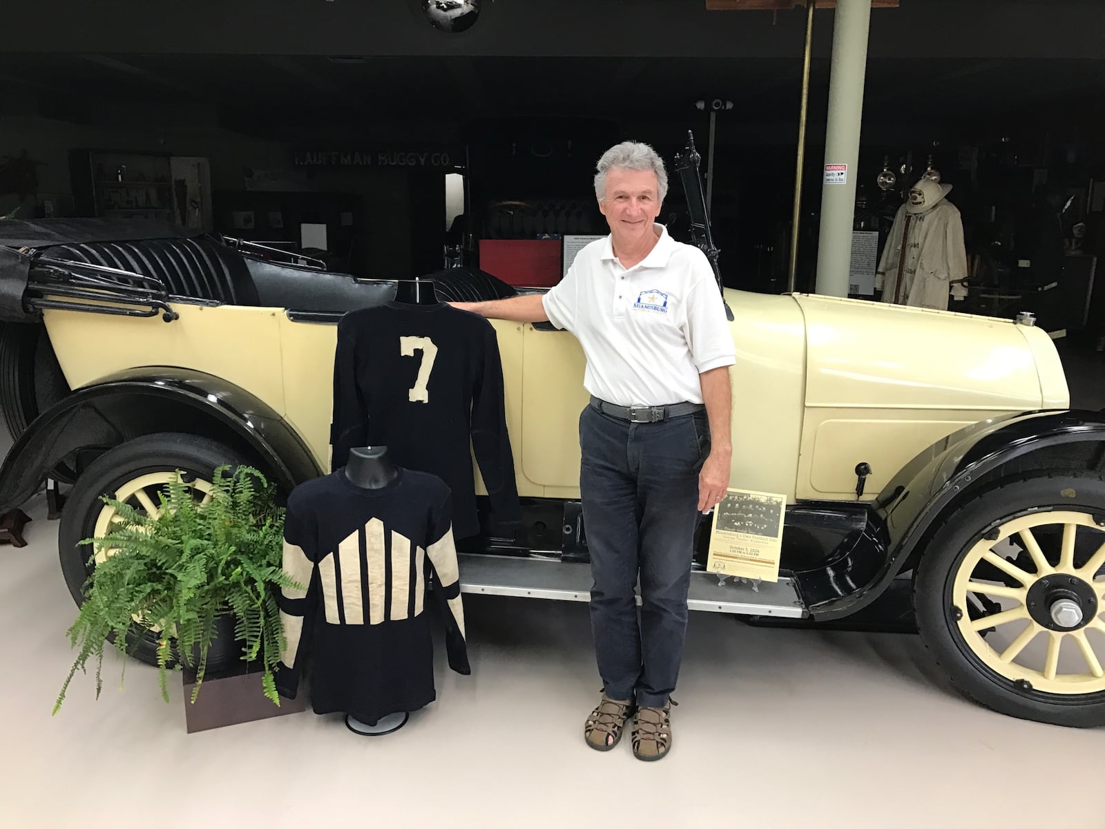 Kim Izor, the curator of the Miamisburg Historical Society, stands next to Hobby Kinderdine’s original wool Dayton Triangles game jerseys. Behind him is a 1918 Willys  Knight 88-4, a popular car during the era that saw the Triangles become one of the NFL’s initial 14 franchises. The display is part of an exhibit celebrating Hobby Kinderdine October 5 at the Miamisburg History Center. Tom Archdeacon/CONTRIBUTED