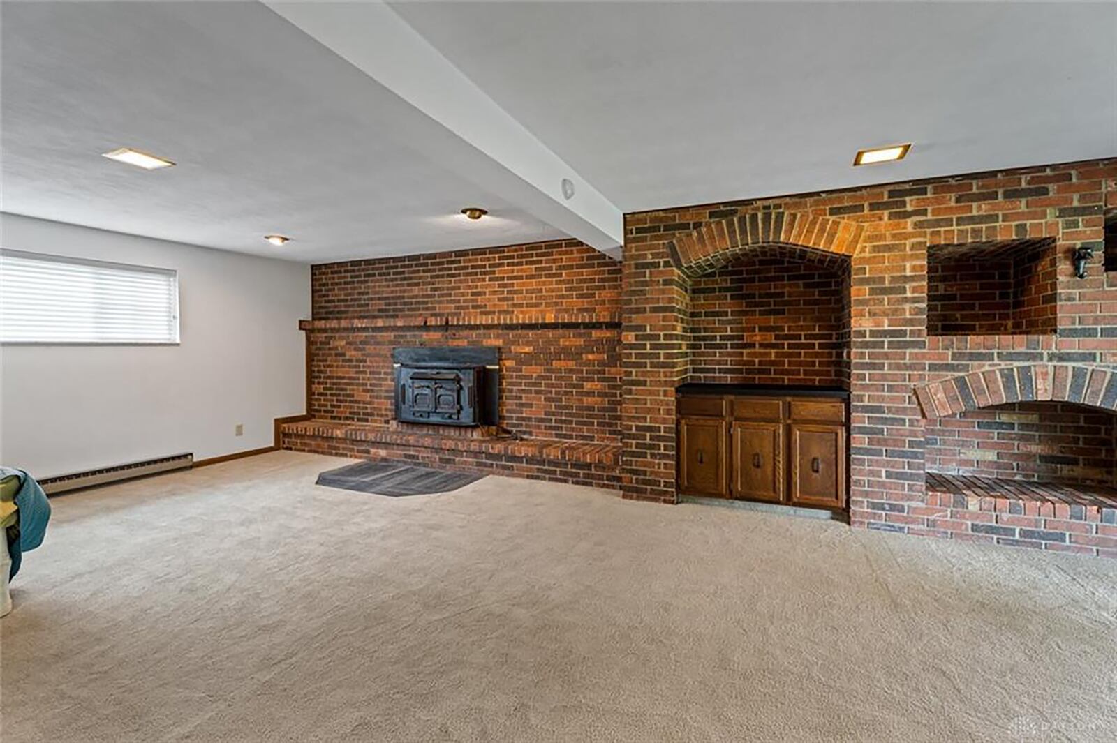 Lower level family room has neutral carpeting, beamed ceiling, brick wall with woodburning stove and built in bar and storage alcoves. The basement walks out to the rear of the home.