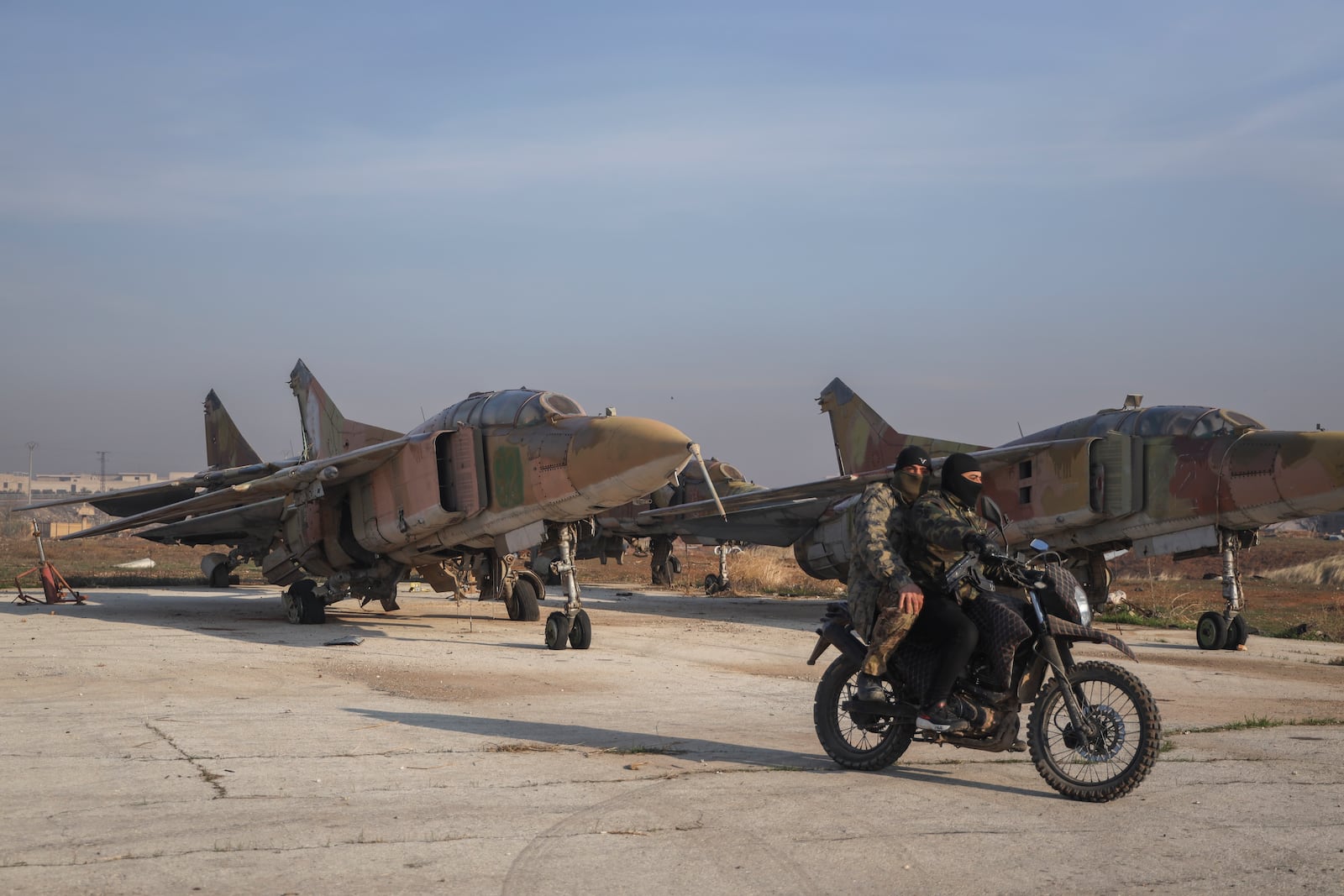 Syrian opposition fighters ride on a motorcycle past Syrian army planes at the Al-Nayrab military airport after they took control of the facility in the outskirts of Aleppo, Syria, Monday, Dec. 2, 2024. .(AP Photo/Omar Albam)