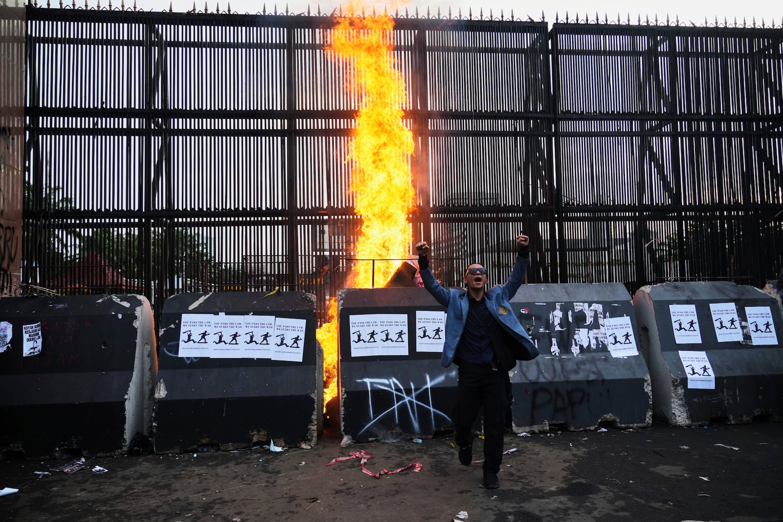 A protester shout slogans as a fire burns during a rally outside the parliament in Jakarta, Indonesia, Thursday, March 20, 2025, against the passing of a controversial revision of a military law that will allow military officers to serve in more government posts without resigning from the armed forces. (AP Photo/Tatan Syuflana)