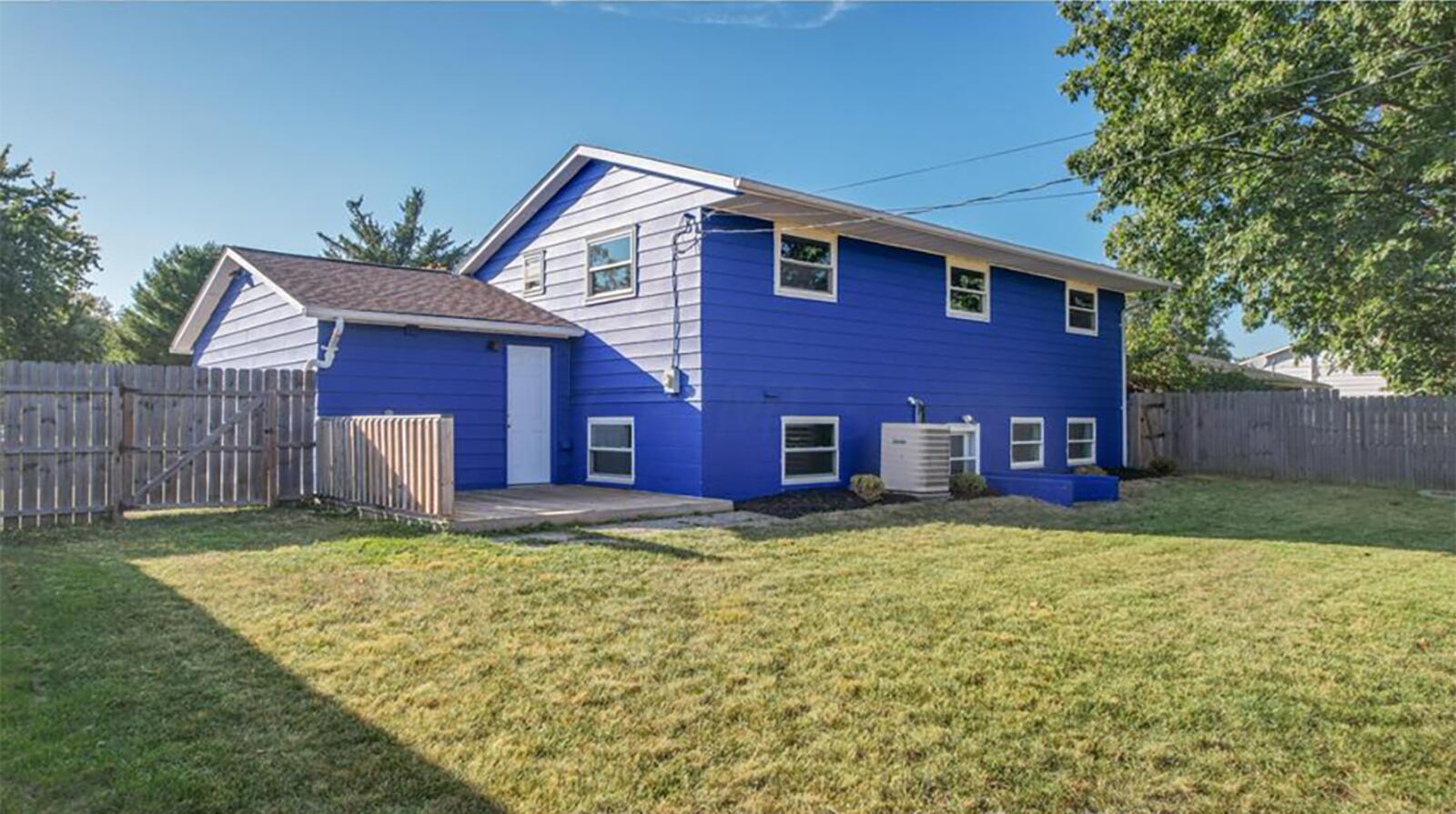 The rear of the home features two exterior doors, a wood privacy fence, a wood deck with railing and a storage shed. Contributed