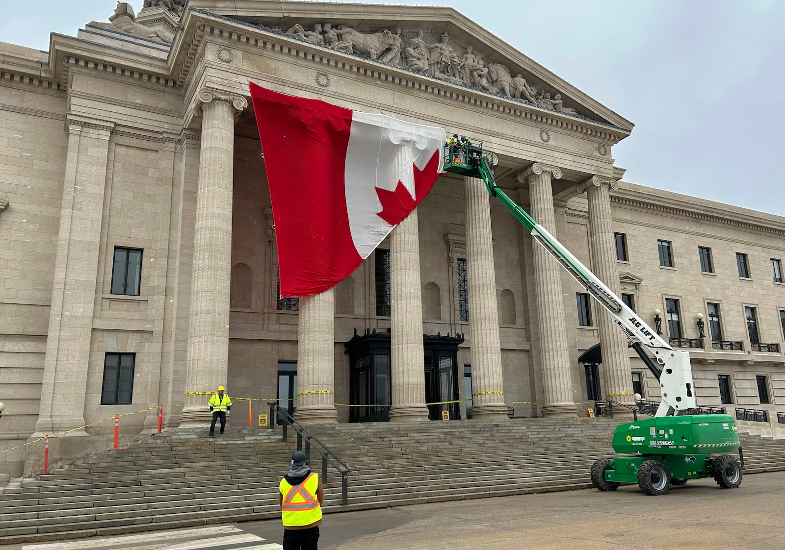 Workers install a large Canadian flag on the front of the Manitoba legislative building in Winnipeg on Tuesday March 4, 2025. (Steve Lambert/The Canadian Press via AP)