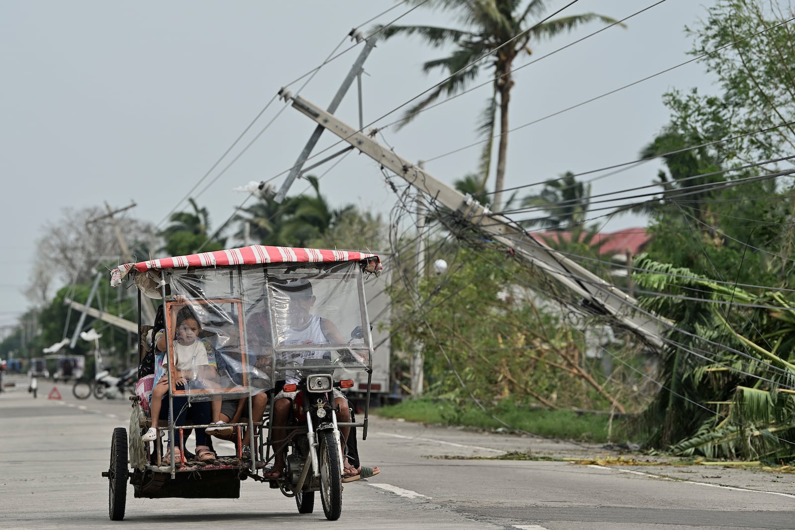 Residents riding a tricycle pass by toppled electrical posts caused by Typhoon Yinxing, locally called Marce, in Camalaniugan, Cagayan province, northern Philippines on Friday Nov. 8, 2024. (AP Photo/Noel Celis)