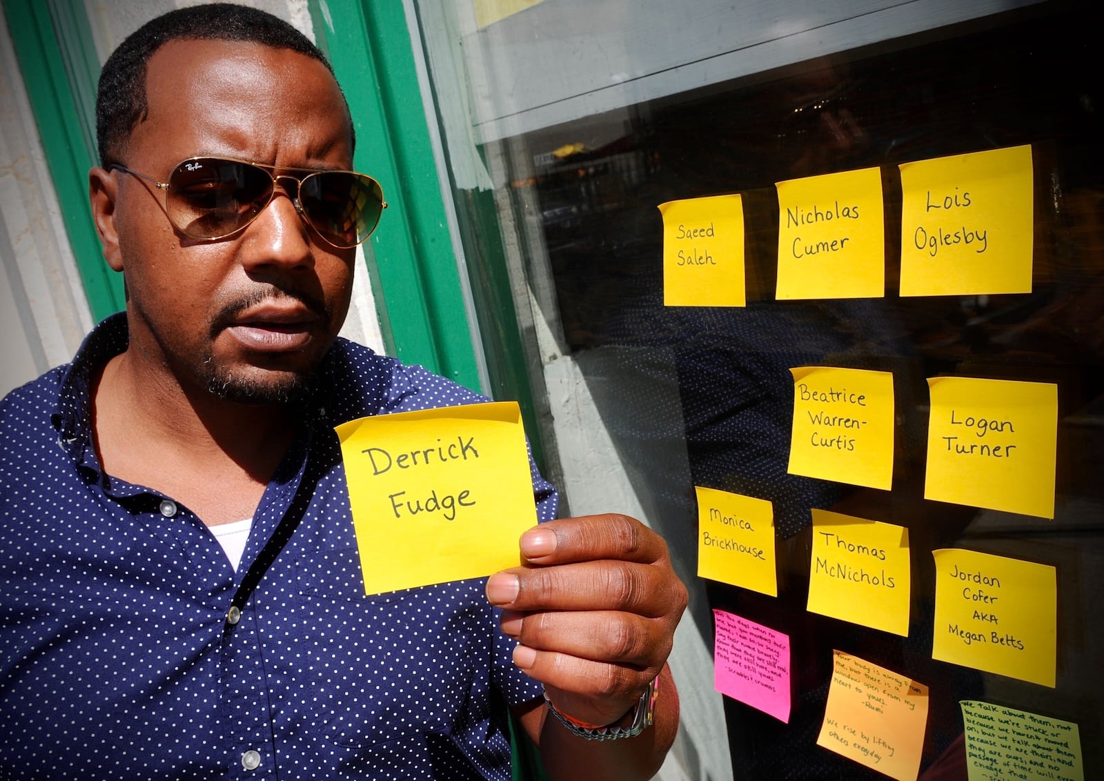 Dion Green’s father Derrick Fudge was one of the victim’s of the Oregon Street shooting two years ago holds up a post-it note with his father’s name that someone had left with the other names for victims on a window on Fifth St., Tuesday, August 2, 2021. MARSHALL GORBY\STAFF