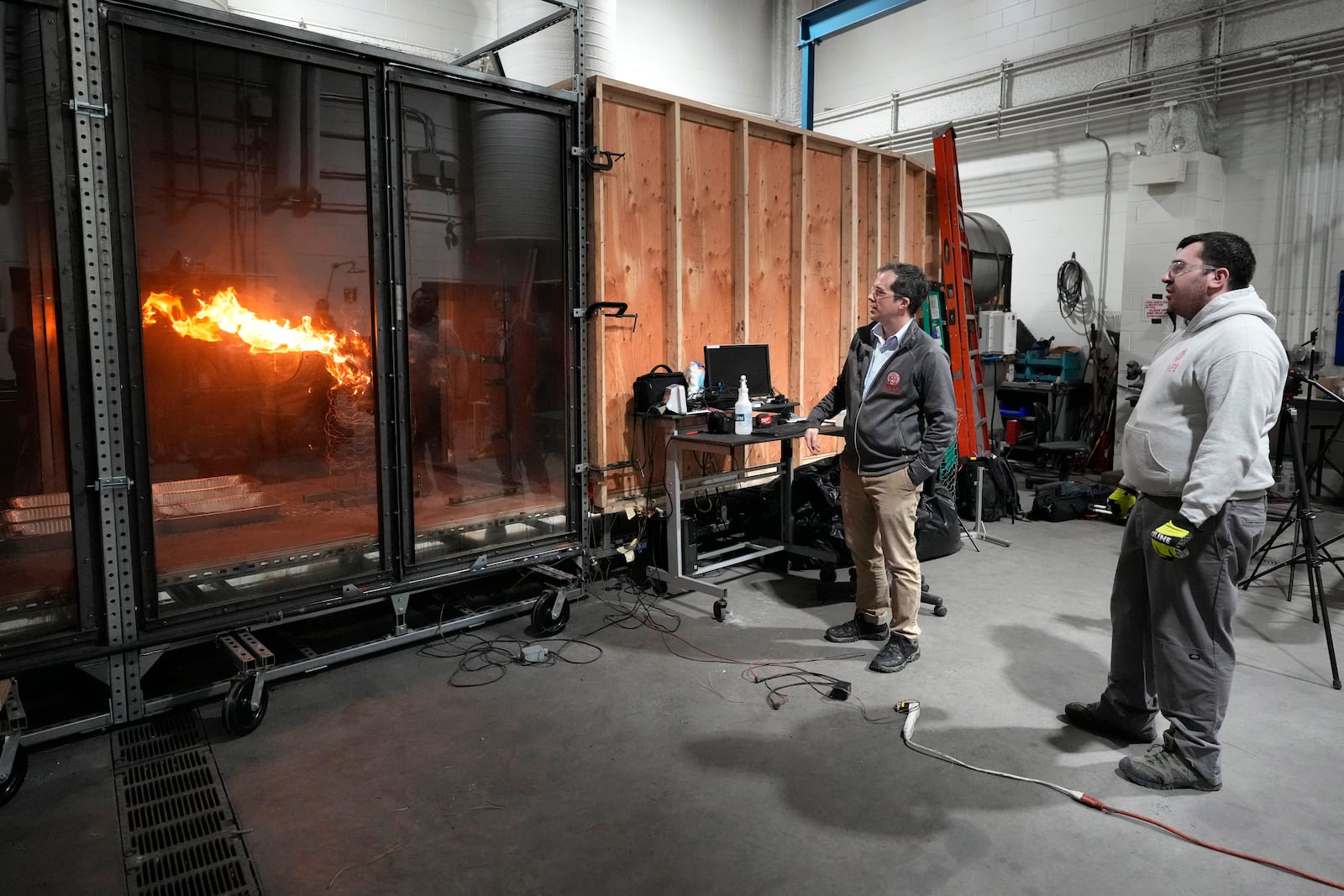 James Urban, assistant professor in the department of Fire Protection Engineering at Worcester Polytechnic Institute, left, and Fernando Ebensperger, a PhD student, watch brush burn in a wind tunnel, Wednesday, Jan. 15, 2025, in Worcester, Mass. (AP Photo/Robert F. Bukaty)