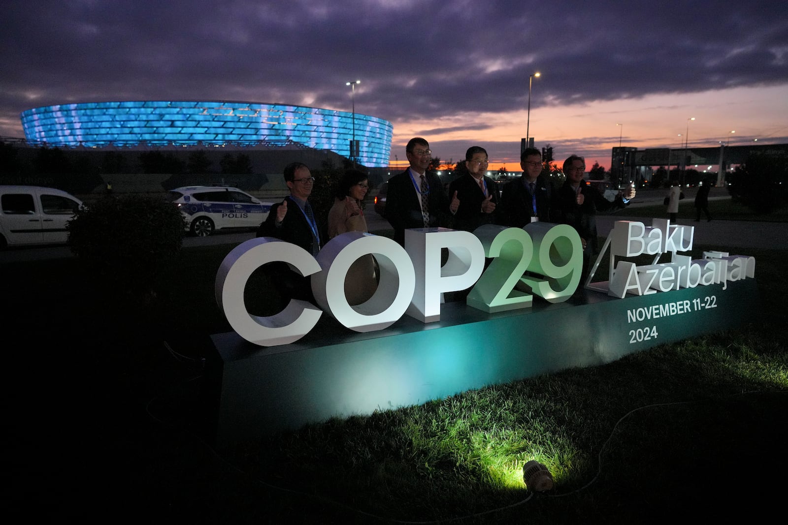 People pose for a photo with the Baku Olympic Stadium in the background at the COP29 U.N. Climate Summit, Thursday, Nov. 14, 2024, in Baku, Azerbaijan. (AP Photo/Peter Dejong)