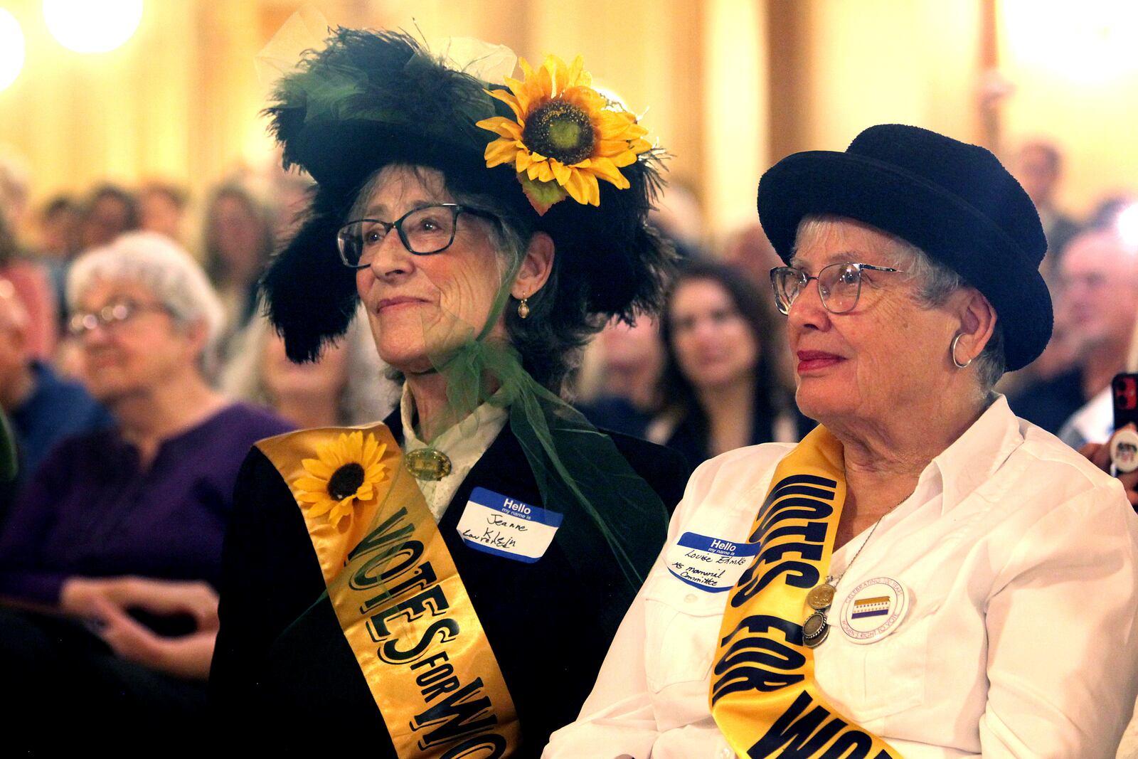 Jeanne Klein, left, a retired University of Kansas professor who researched the women's voting rights movement in Kansas, and Louise Ehmke, right, a member of the Kansas Suffragist Memorial Committee, watch a ceremony ahead of the unveiling of a new Statehouse mural honoring suffragists, Wednesday, Jan. 29, 2025, in Topeka, Kan. (AP Photo/John Hanna)