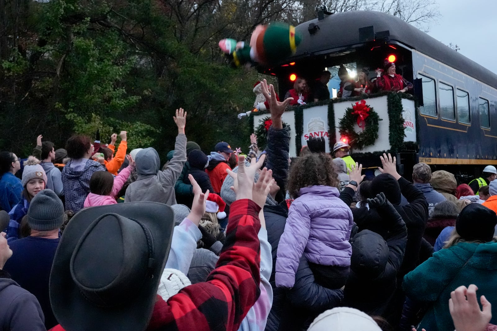 People reach for toys tossed from the CSX Santa Train, Saturday, Nov. 23, 2024, in Elkhorn City, Ky. The train brings presents to small towns along a 110-mile portion of the railroad line in rural Appalachian Tennessee, Kentucky and Virginia. (AP Photo/George Walker IV)