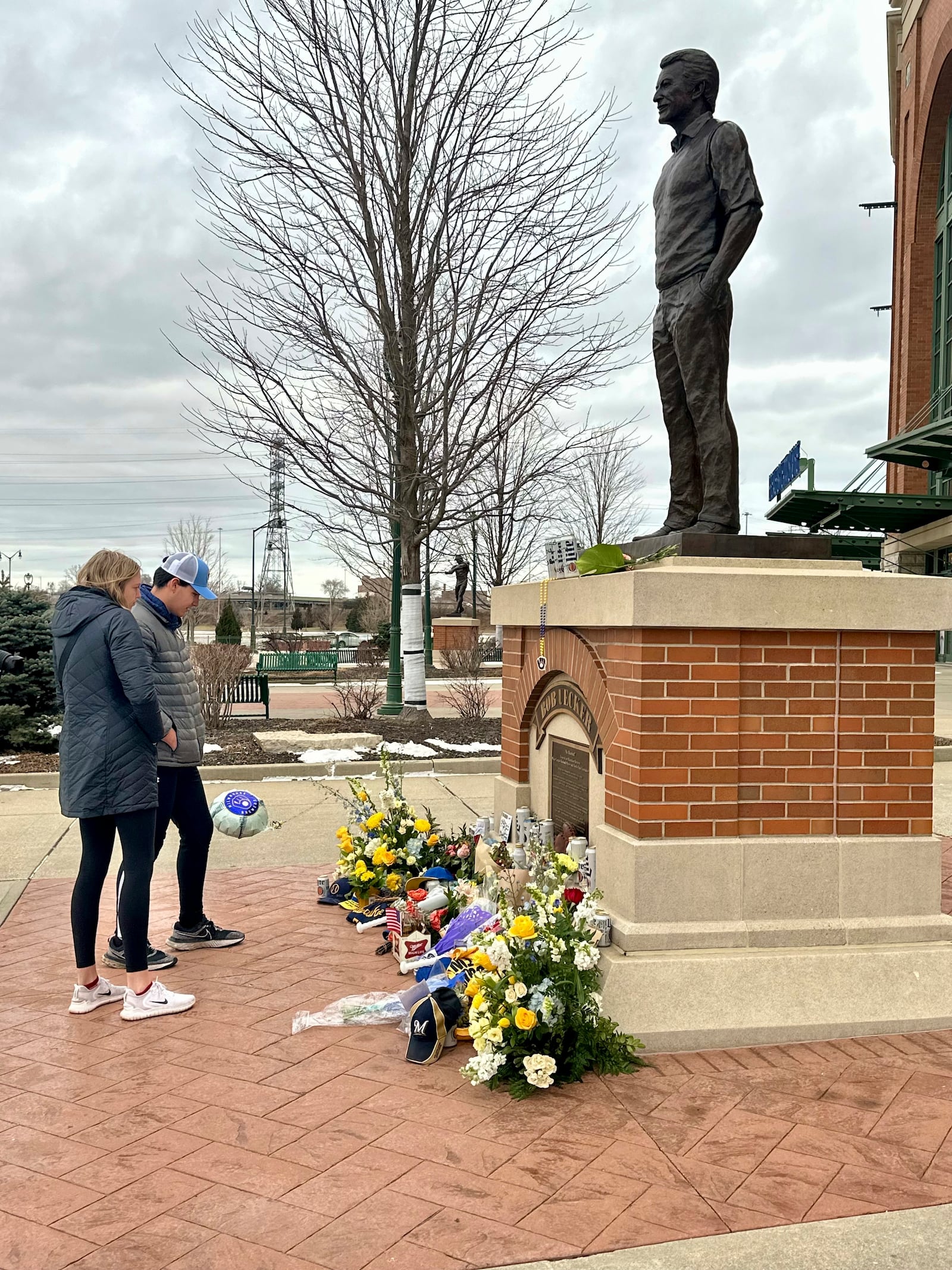 E.J. Kuster, right, and Deanna White, both of Milwaukee, pay their respects at a statue honoring Bob Uecker outside American Family Field in Milwaukee, Thursday, Jan. 16, 2025. (AP Photo/Steve Megargee)