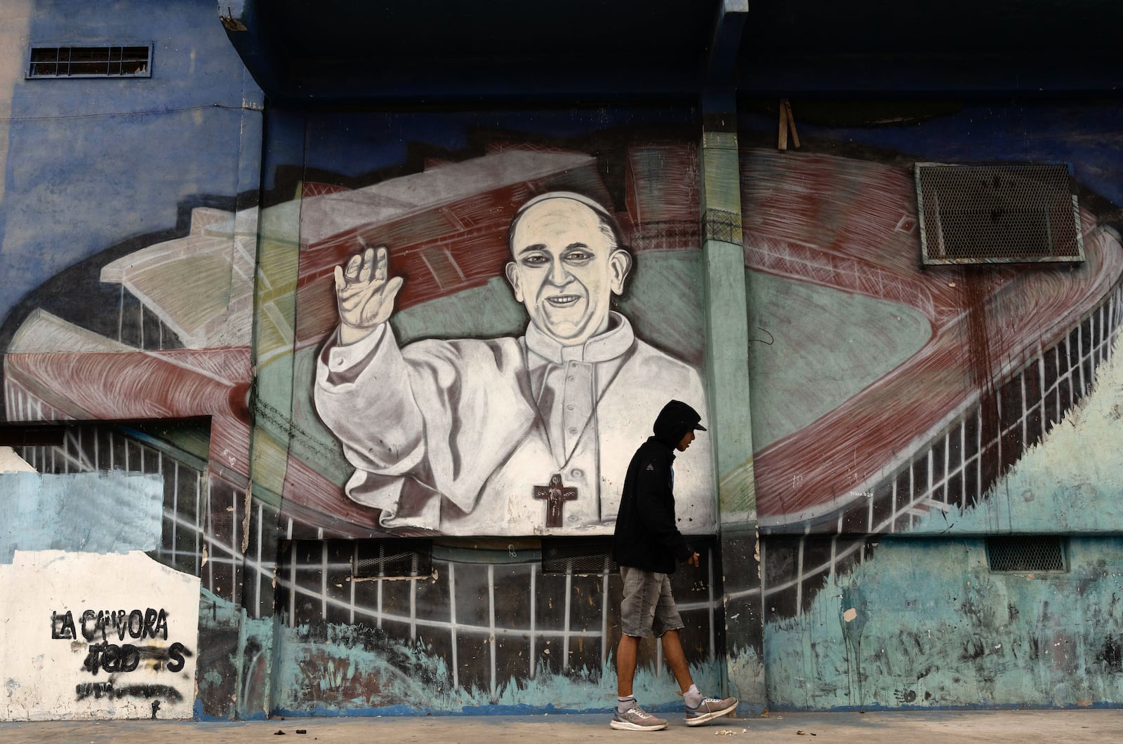 A man walks past a mural of Pope Francis at the stadium of San Lorenzo, his soccer team, in the Padre Ricciardelli neighborhood of Buenos Aires, Argentina, Tuesday, Feb. 25, 2025. (AP Photo/Rodrigo Abd)