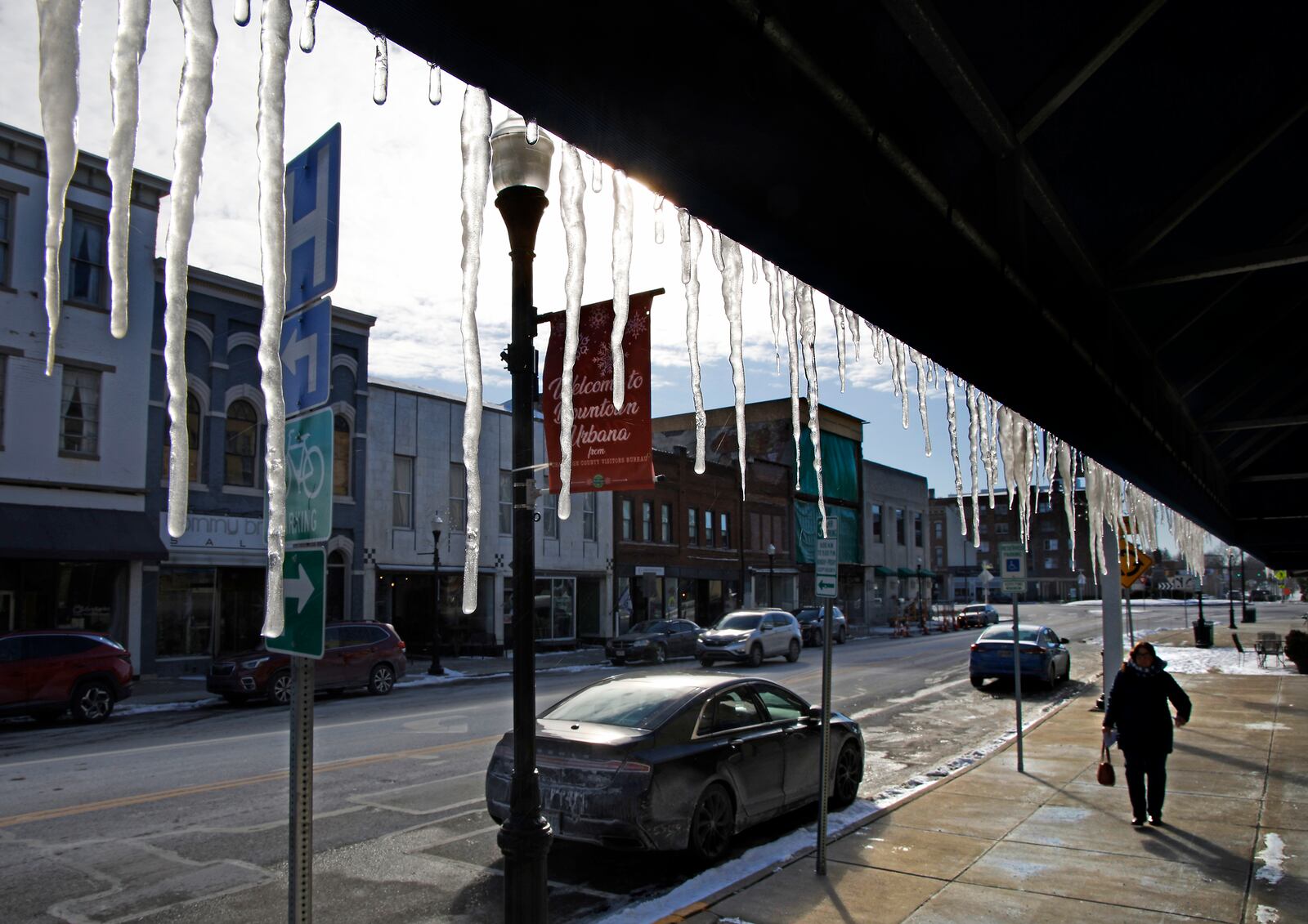 A woman walks under a row of icicles hanging off an awning in front of Farmers & Merchant's State Bank along Main Street in Urbana Wednesday, Jan. 17, 2024. BILL LACKEY/STAFF