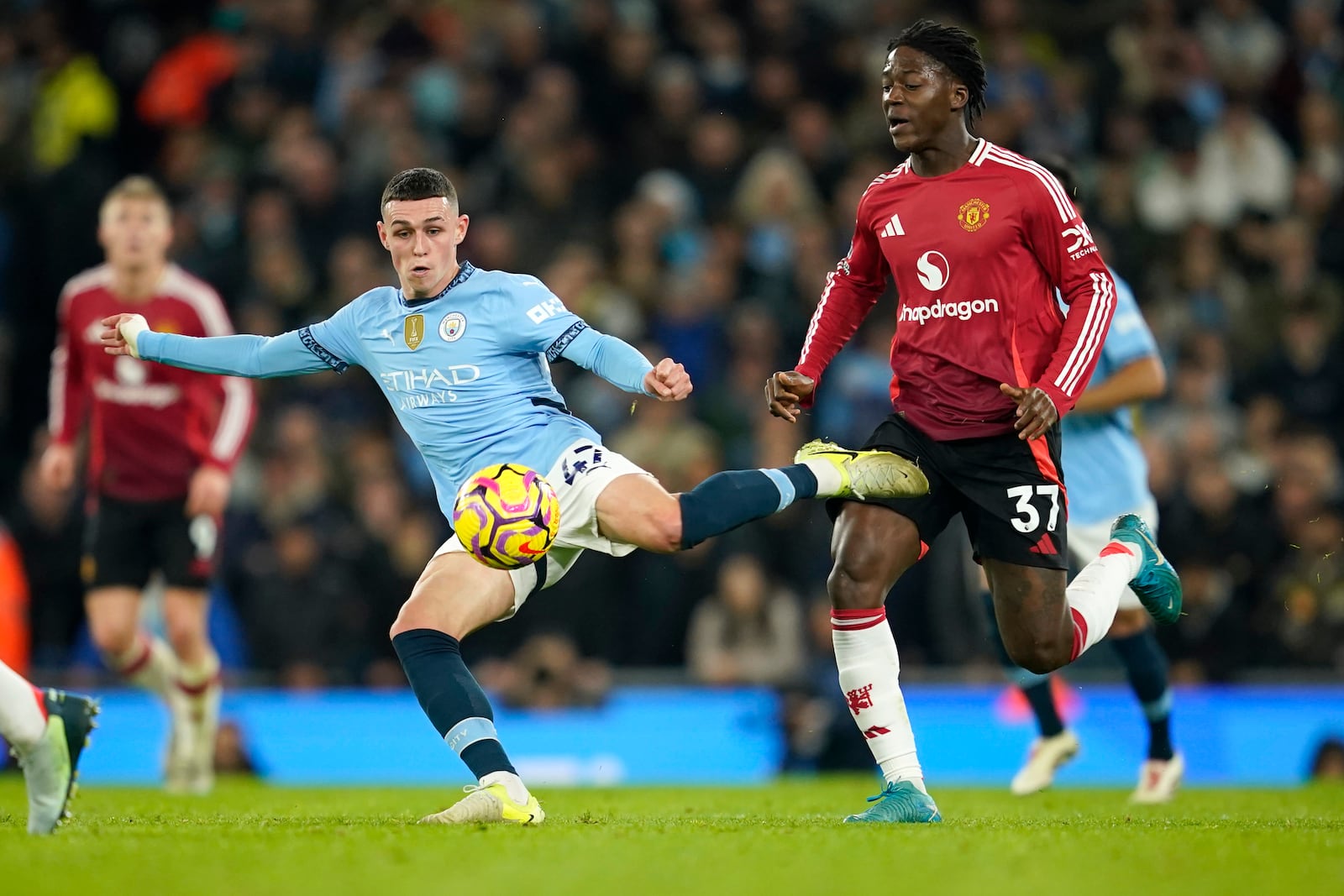 Manchester City's Phil Foden kicks the ball ahead of Manchester United's Kobbie Mainoo during the English Premier League soccer match between Manchester City and Manchester United at the Etihad Stadium in Manchester, Sunday, Dec. 15, 2024. (AP Photo/Dave Thompson)