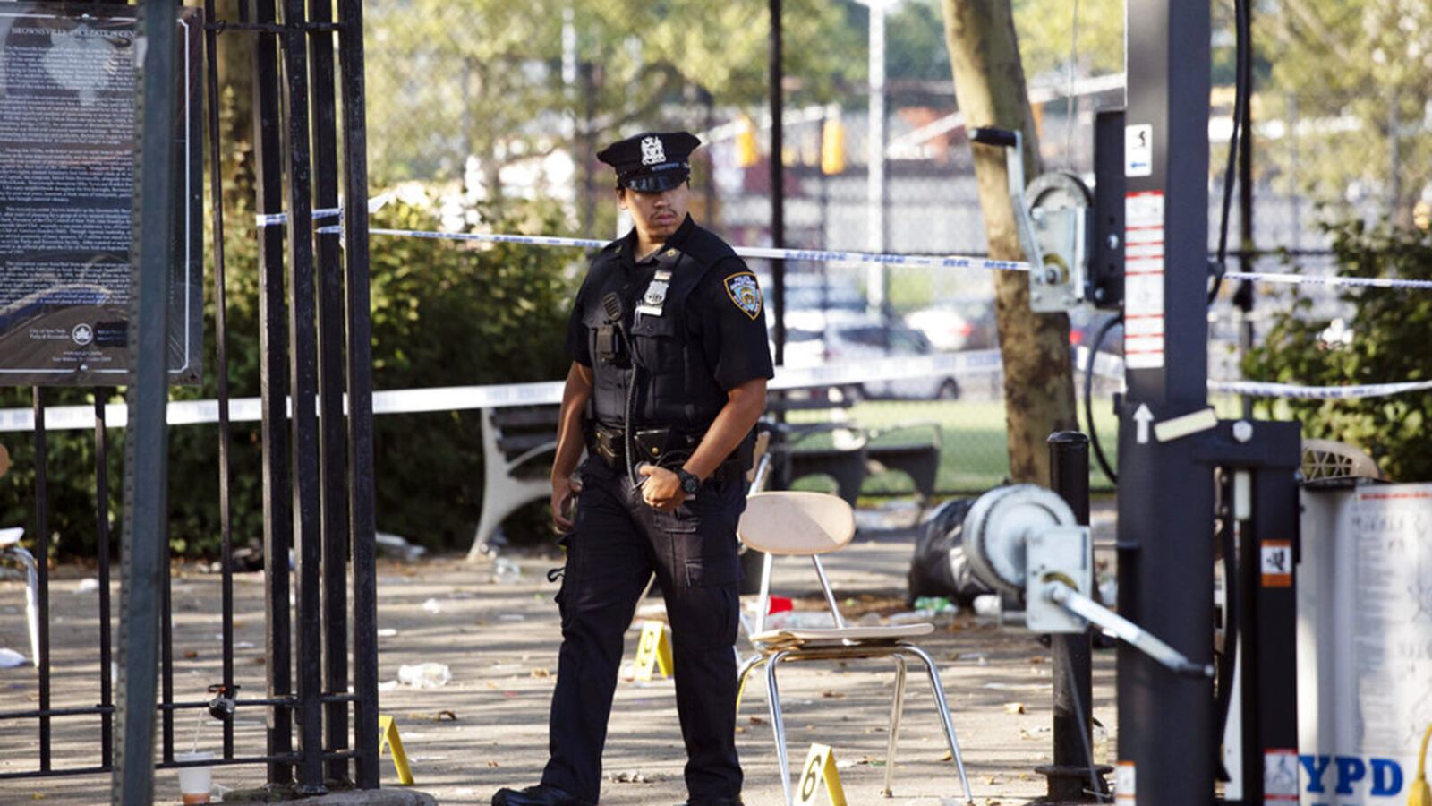 A police officer walks by yellow evidence markers at a playground in the Brownsville neighborhood in Brooklyn, New York, Sunday. Police said one man was killed and at least 11 others were injured in a shooting Saturday.