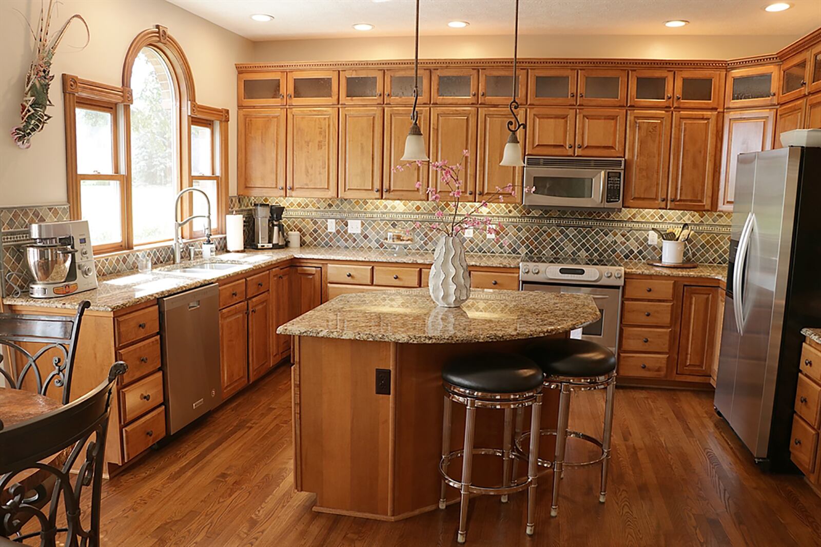 The U-shaped kitchen has an abundance of cabinetry with bubble-glass panel doors along the top of the hanging cabinets. An island has a curved countertop to allow for seating and storage. CONTRIBUTED PHOTO BY KATHY TYLER