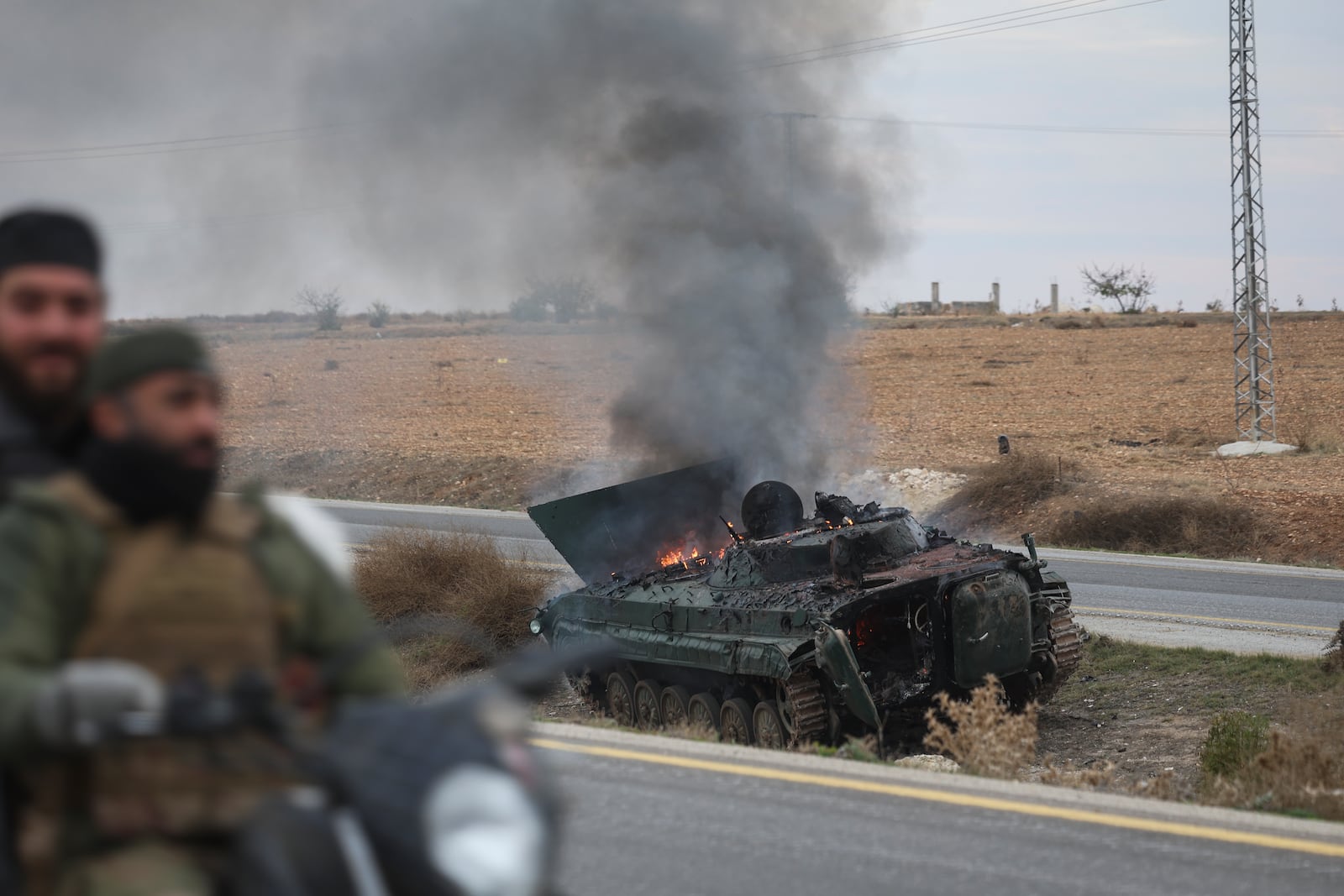 Syrian opposition fighters drive past a burning government armoured vehicle south of Hama, Syria, on Saturday, Dec. 7, 2024. (AP Photo/Ghaith Alsayed)