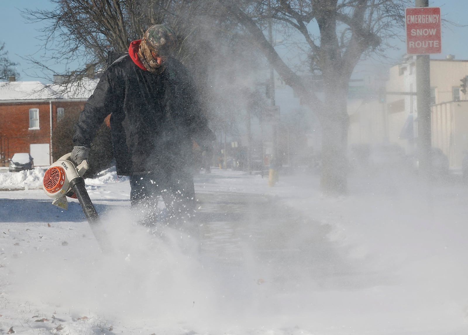 Dyelan Youngblood, from Courtryside Land and Lawn, braves the cold as he uses a leaf blower to clean the snow off the sidewalk along Main Street in Springfield Tuesday, Jan. 16, 2024. Youngblood said he uses a leaf blower when the snow is light and not wet. BILL LACKEY/STAFF