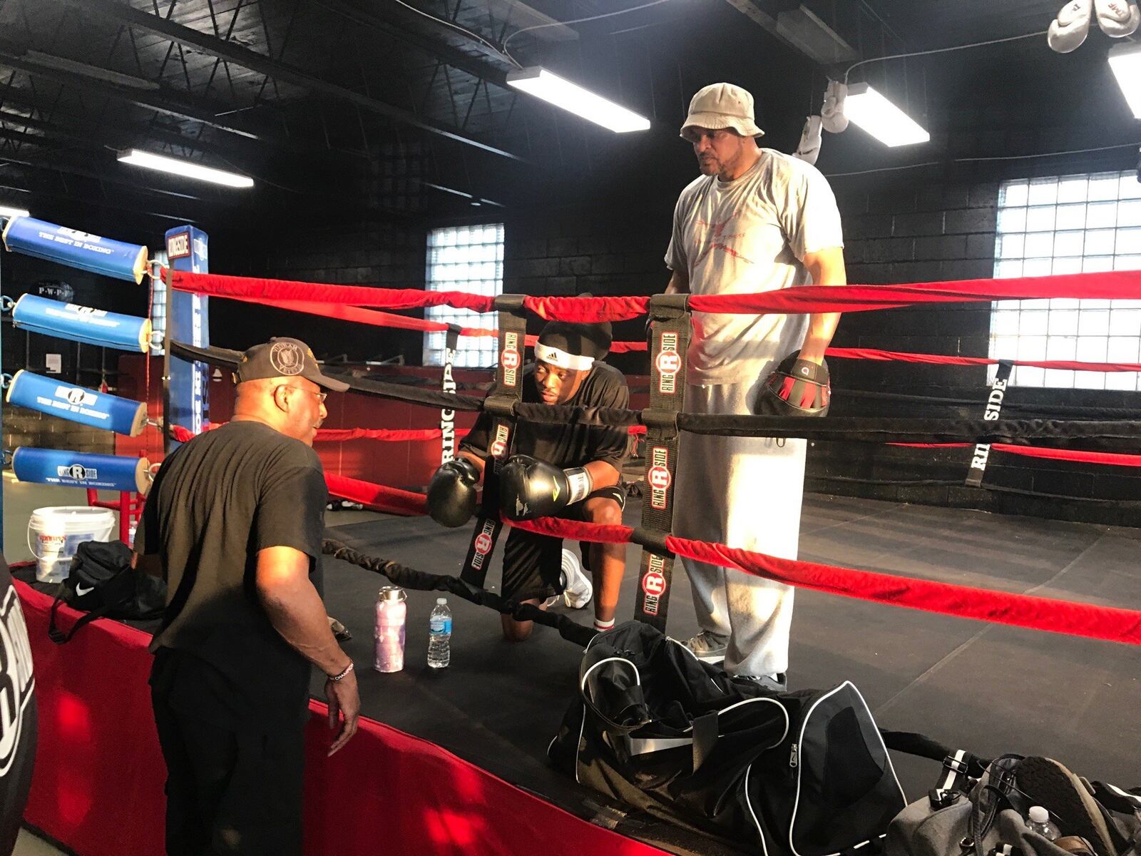 Mike Evans (kneeling) gets some advice from his longtime trainer Ron Daniels (left) as co-trainer Craig Thurmond watches from ring at M-Power Gym. Tom Archdeacon/STAFF