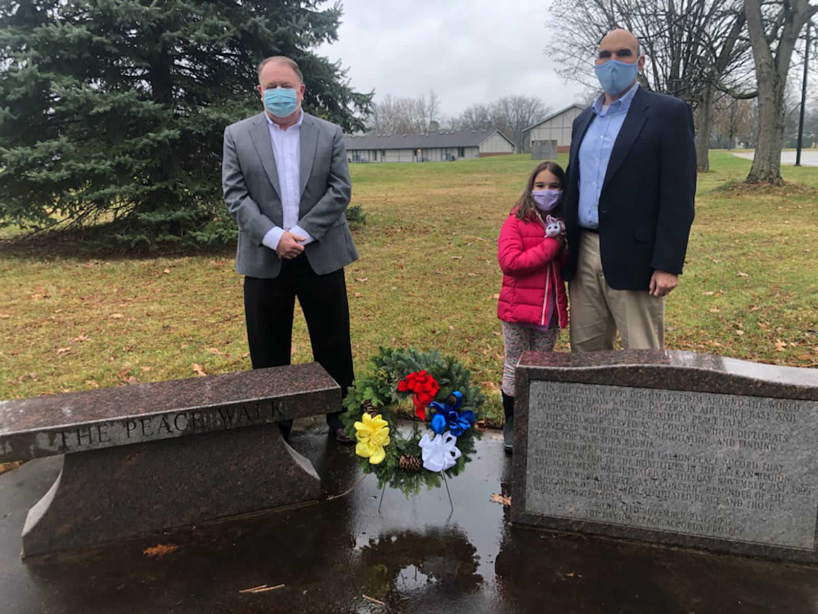 Retired Air Force Lt. Col. John McCance (left) and Matt Joseph, Dayton city commissioner, take part in a private wreath-laying ceremony Nov. 21, 2020, at the Peace Walk bench and plaque on Wright-Patterson Air Force Base to commemorate the 25th anniversary of the Dayton Peace Accords, which ended the brutal Bosnian War. The two serve as co-chairs of the anniversary events committee. Also pictured is Joseph’s daughter, Sara. In 1995, the peace talks unfolded over 20 days at Hope Hotel (now the Hope Hotel and Richard C. Holbrooke Conference Center.) The accords were signed in Paris on Dec. 14 that year, which ended civil war and genocide in Bosnia-Herzegovina, a small southeast European country once part of Yugoslavia. COURTESY PHOTO/DONNA SCHLAGHECK