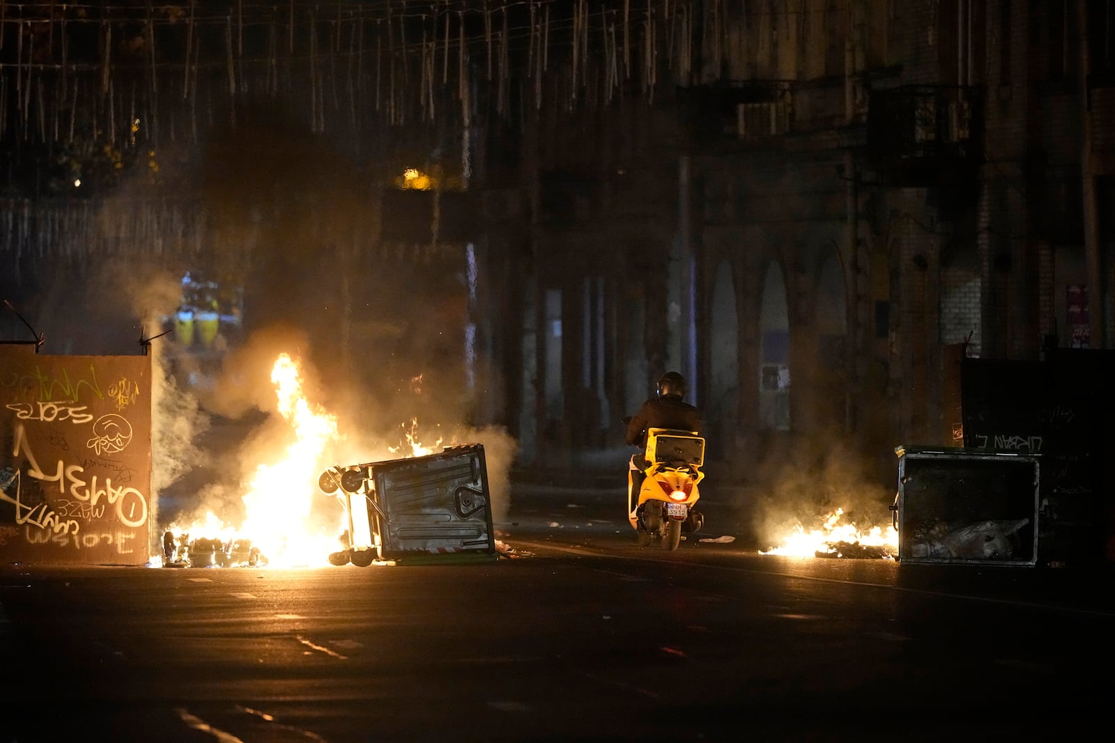 A motorcyclist passes a burning barricade during a rally to protest against the government's decision to suspend negotiations on joining the European Union in Tbilisi, Georgia, early Wednesday, Dec. 4, 2024. (AP Photo/Pavel Bednyakov)