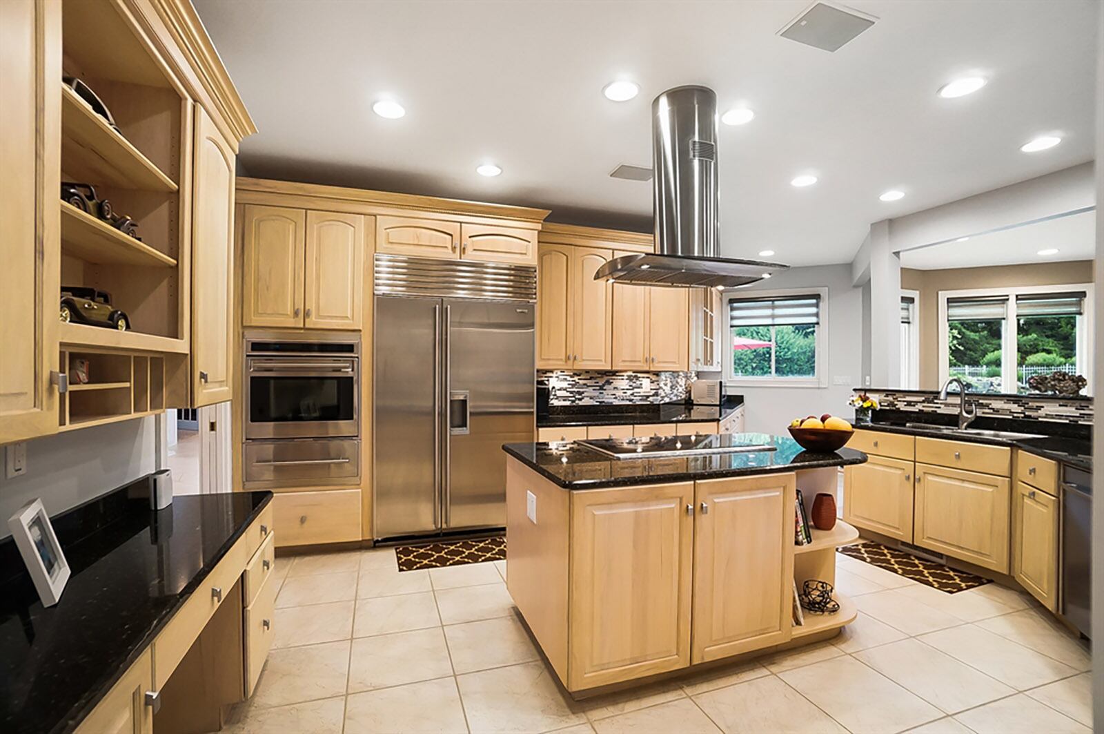 Light maple cabinets complement the kitchen’s dark granite countertops. A stainless-steel hood-vent hangs above the island, which has a cooktop and wall ovens are close by. CONTRIBUTED PHOTO