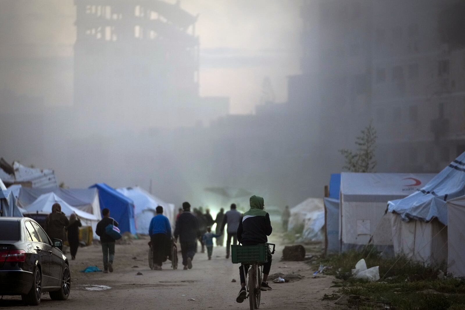 Surrounded by smoke from a nearby Israeli army strike, Palestinians walk past tents in central Gaza City on Saturday, March 22, 2025. (AP Photo/Jehad Alshrafi)