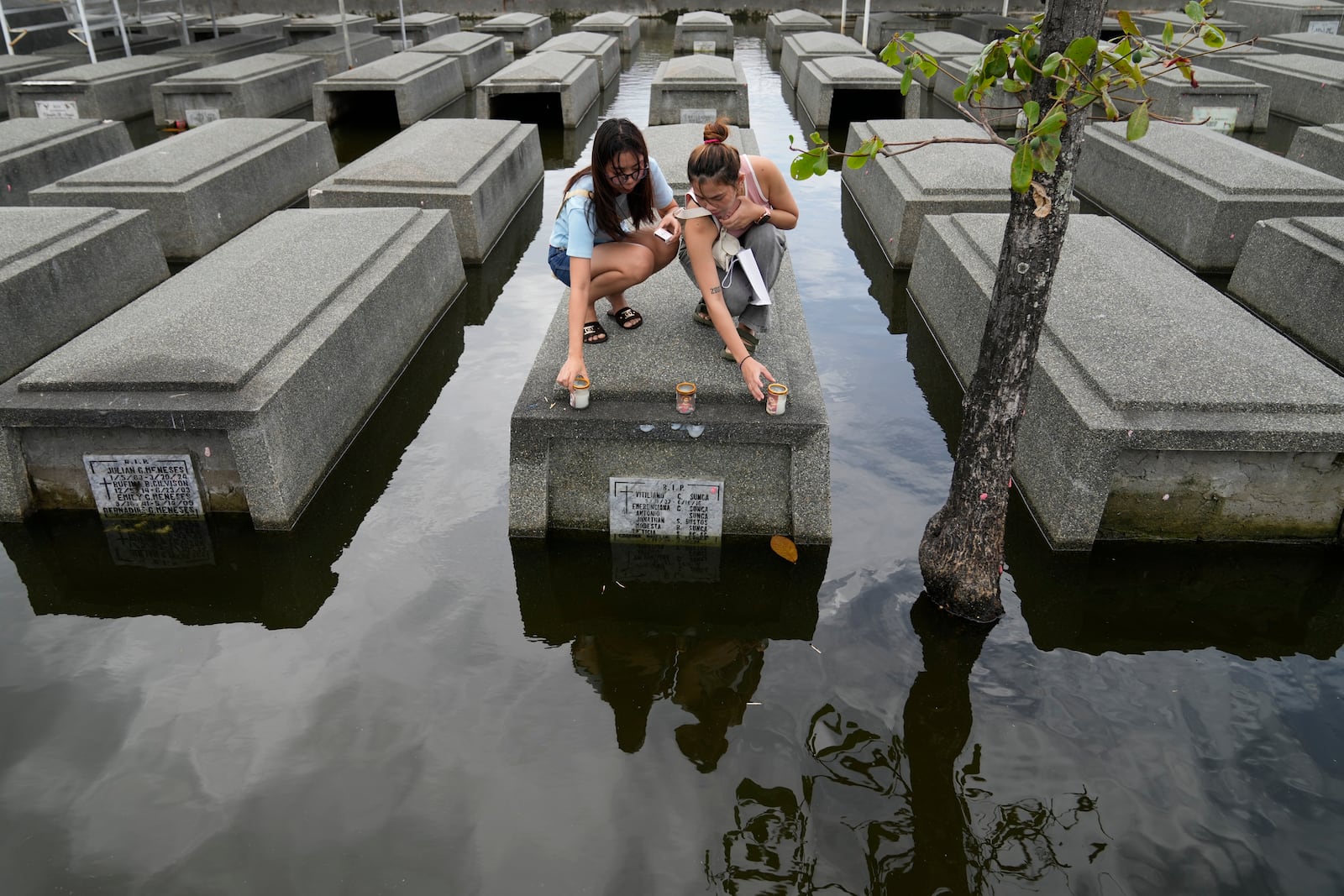 Women places candles on the half-submerged tomb of family members at flood-prone Holy Spirit Memorial Park in Masantol, Pampanga province, Philippines after heavy rains from recent tropical storm Trami caused water to become higher than usual, ahead of All Saints Day, Thursday Oct. 31, 2024. (AP Photo/Aaron Favila)