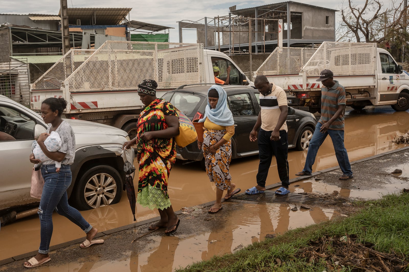 People walk along partially flooded roads, in Mamoudzou, Mayotte, Thursday, Dec. 19, 2024. (AP Photo/Adrienne Surprenant)