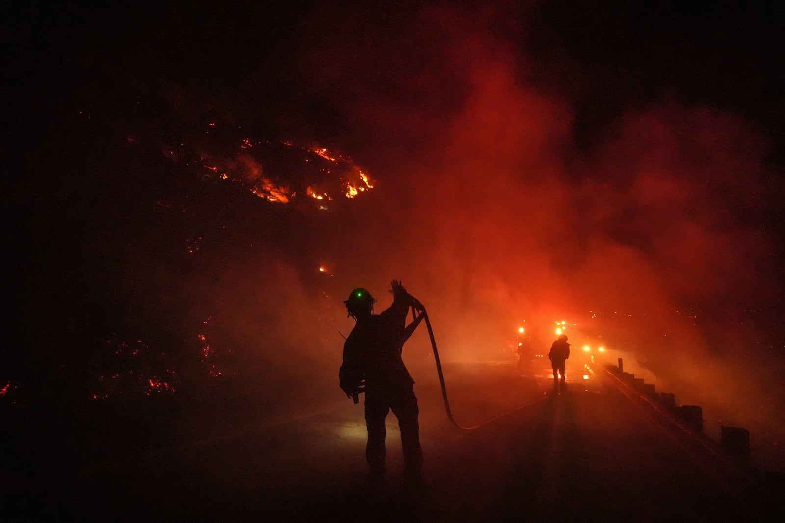 Two firefighters roll up a fire hose during the Lilac Fire in Bonsall, Calif., Tuesday, Jan. 21, 2025. (AP Photo/Jae C. Hong)