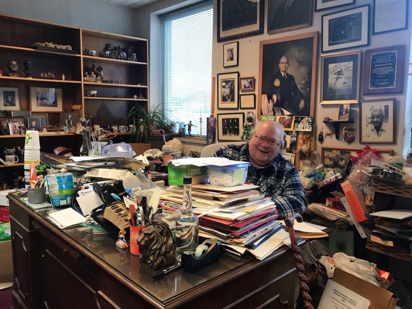 Judge Dan Gehres peeks out from behind the overflow of memorabilia, souvenirs, and sprots collectibles that have accumulated in his 36 years of collecting while on the bench. His son Frank is set to take over his seat on the bench this week and his office – where finding a seat is tough. Judge Gehres’ last day is December 31. Already nine pick-up trucks filled with collectibles has been removed and that’s barely made a debt in the office and several courthouse closets filled with Judge Gehres’ collection. Tom Archdeacon/CONTRIBUTED