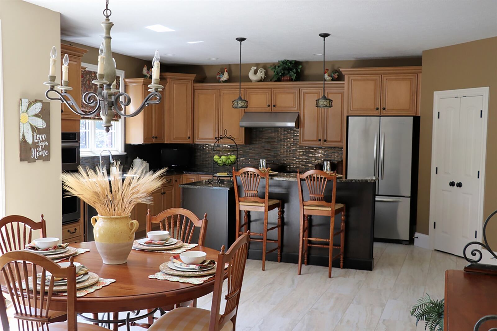 The kitchen has light wood cabinetry with copper-tone mosaic backsplash. A two-level island has breakfast bar seating, work space and storage. Granite countertops provide space for a coffee station. CONTRIBUTED PHOTO BY KATHY TYLER