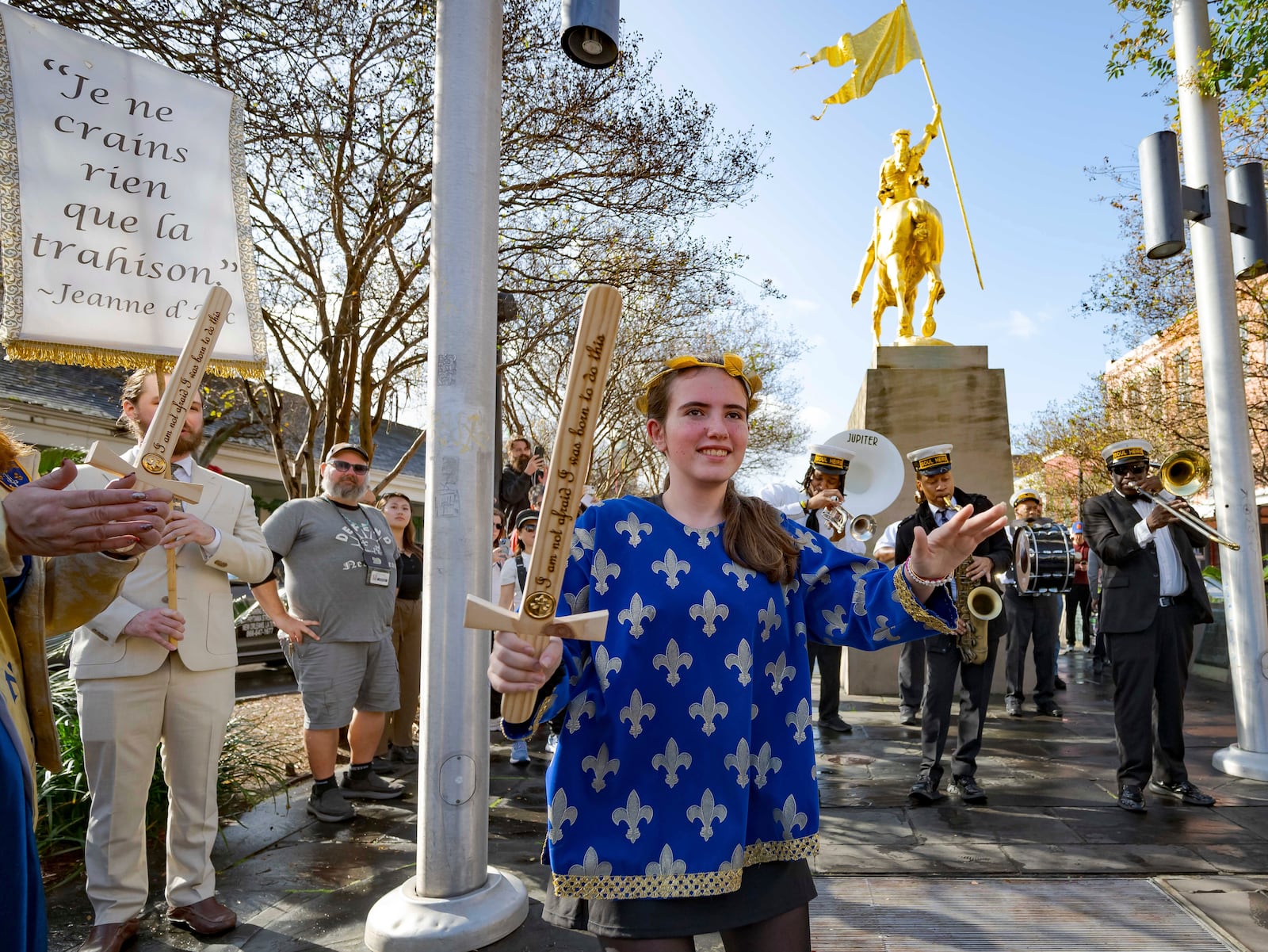 A procession of Krewe de Jeanne d'Arc represented by 2025 Maid of Honor Life Sacco, center, and the Soul Heirs Brass Band dances by a golden statue of St. Joan of Arc in the French Quarter after leaving St. Louis Cathedral in New Orleans, Sunday, Jan. 5, 2025, after a mass honoring victims of the New Year's Day deadly truck attack and shooting not far from the cathedral in the French Quarter. (AP Photo/Matthew Hinton)