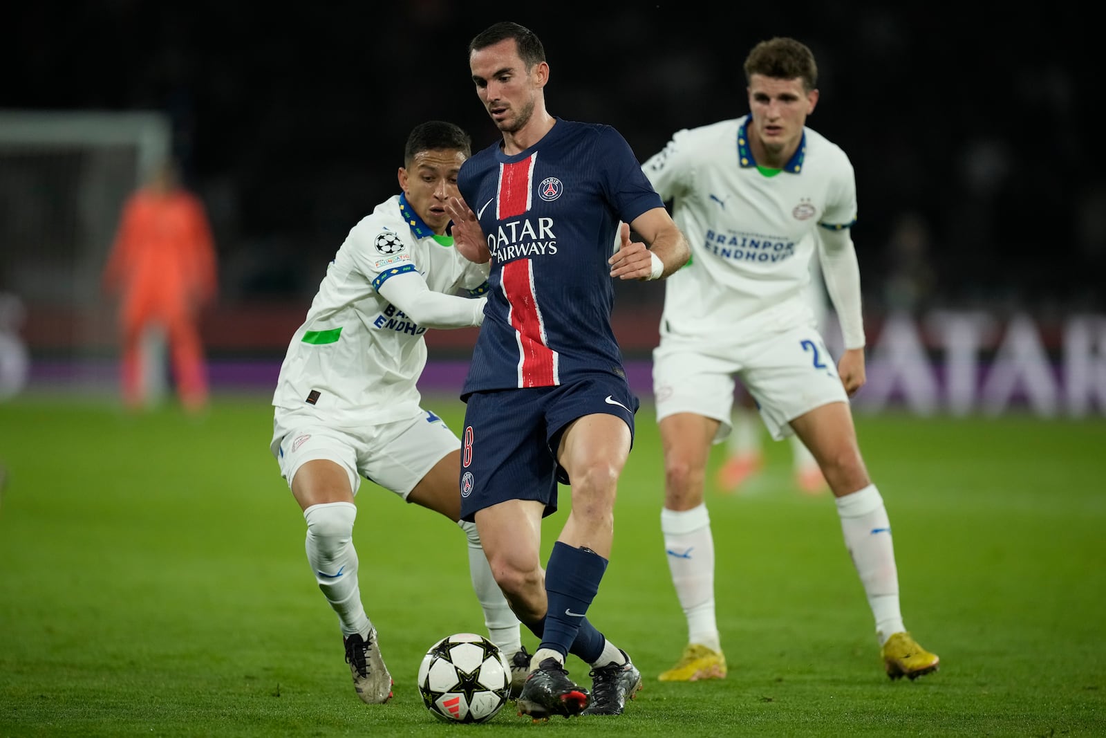 PSG's Fabian Ruiz, center, dribbles PSV's Mauro Junior, left, during the Champions League opening phase soccer match between Paris Saint-Germain and PSV Eindhoven at the Parc des Princes stadium in Paris, France, Tuesday, Oct. 22, 2024. (AP Photo/Christophe Ena)