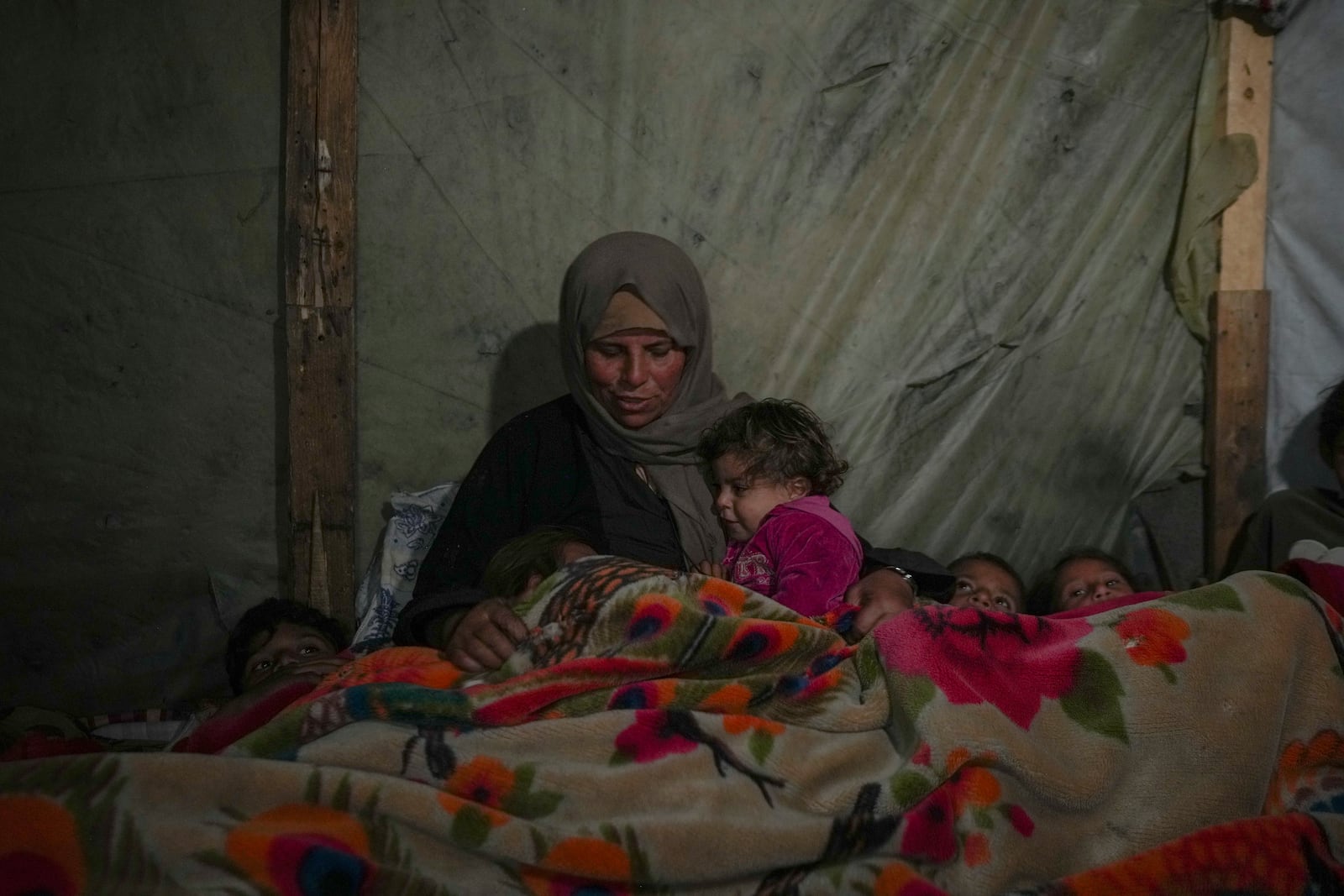 Reda Abu Zarada wraps herself and her grandchildren in blankets as they prepare to sleep in their tent at a camp in Khan Younis, Gaza Strip, Thursday Dec. 19, 2024. (AP Photo/Abdel Kareem Hana)